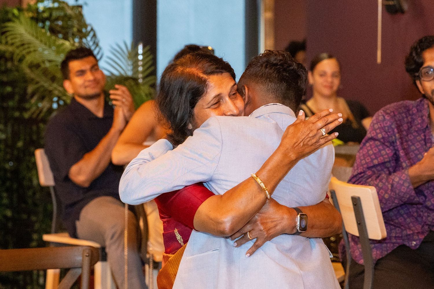 Two guests sharing a warm embrace during an emotional moment at an indoor birthday party celebration.