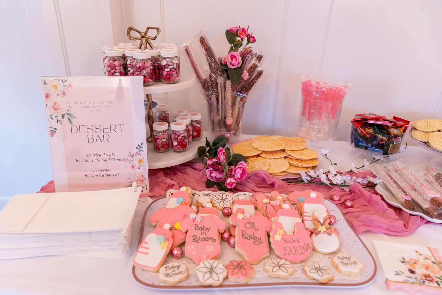 Pink baby shower dessert bar with decorated cookies, jars, and sweet treats display.