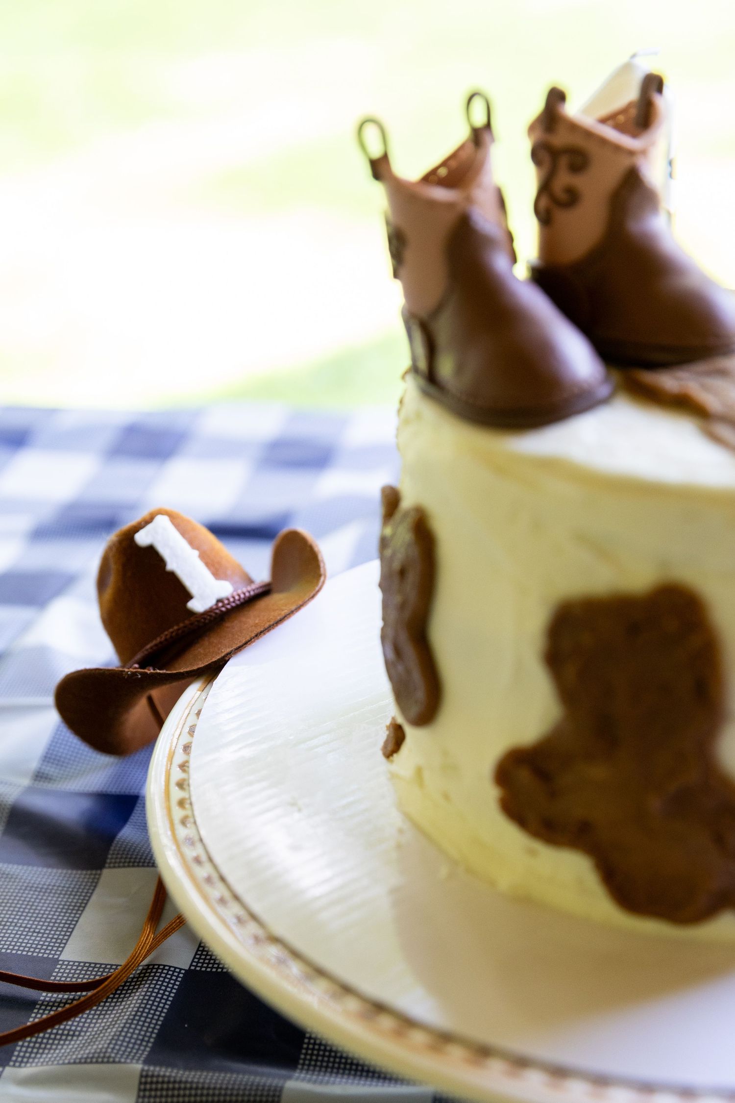 Cowboy-themed first birthday cake with fondant boots, hat, and cow print decorations.