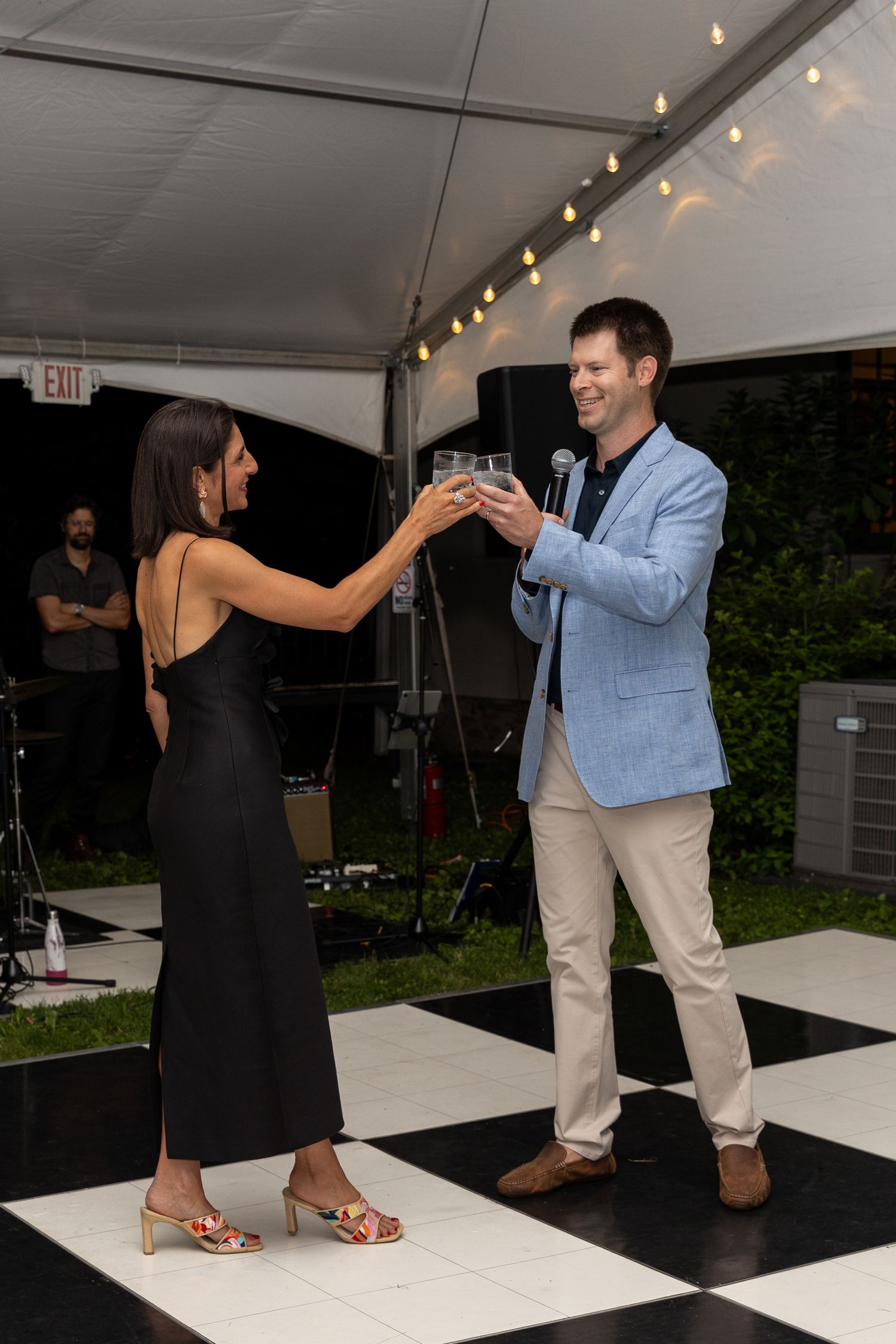 Couple toasting with drinks on a black and white checkered dance floor under a party tent.