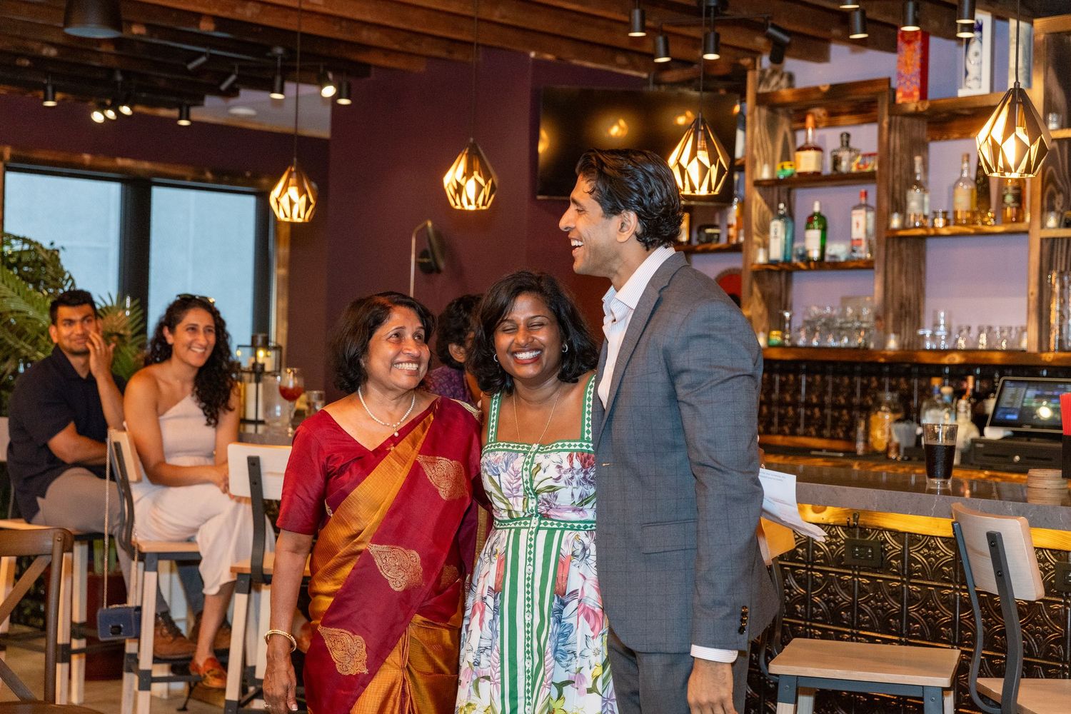 Two women and a man posing together smiling at a restaurant bar during a birthday celebration.