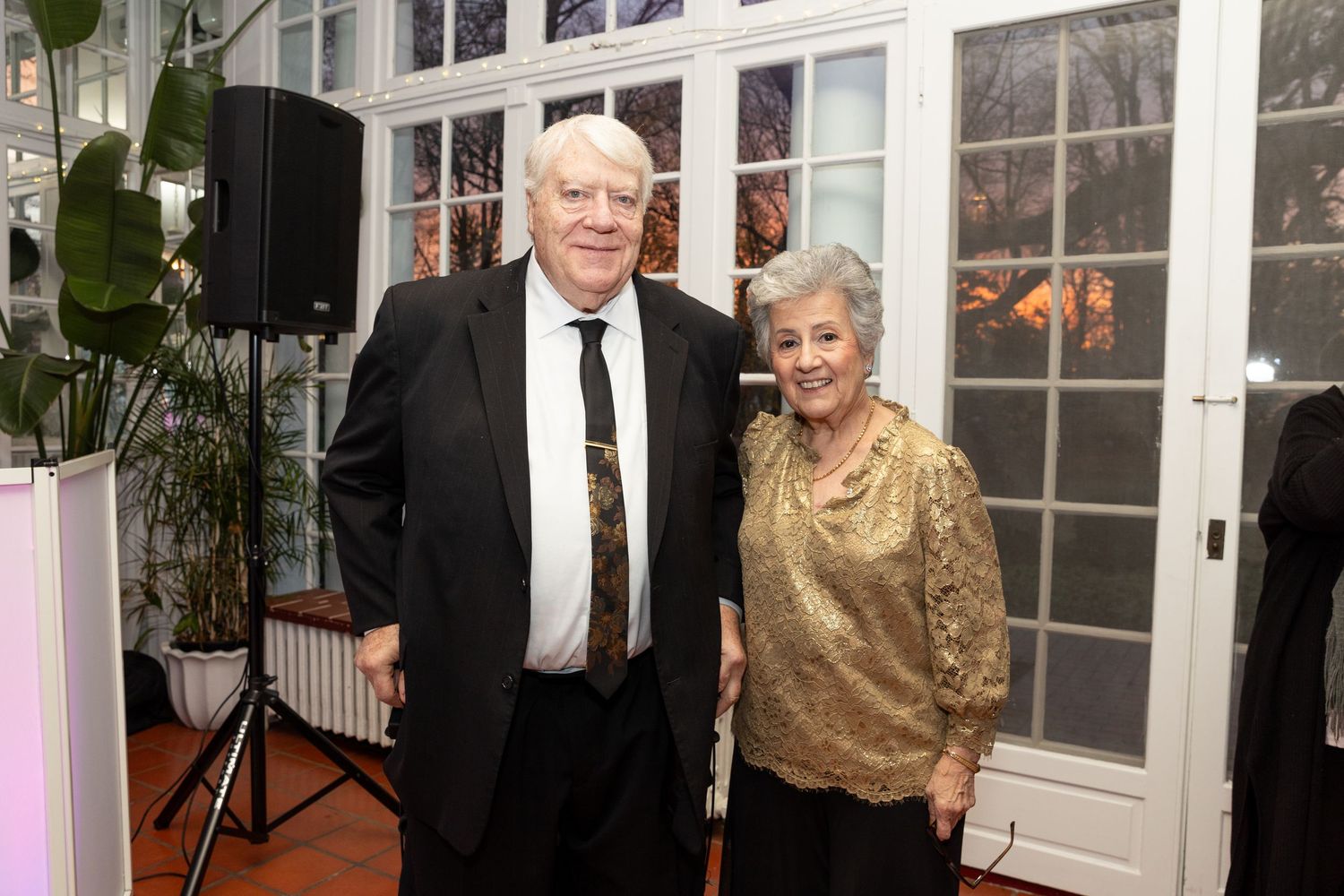 Elderly couple smiling together at formal anniversary celebration in elegantly decorated venue.