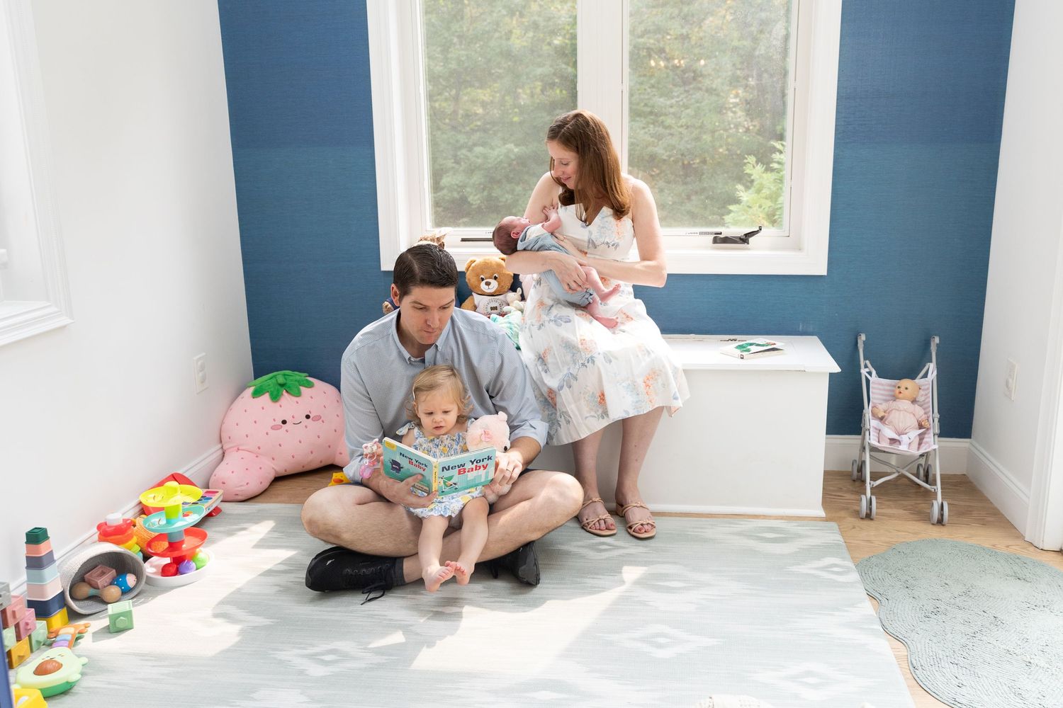Young family with toddler and newborn relaxing together in a blue nursery room.
