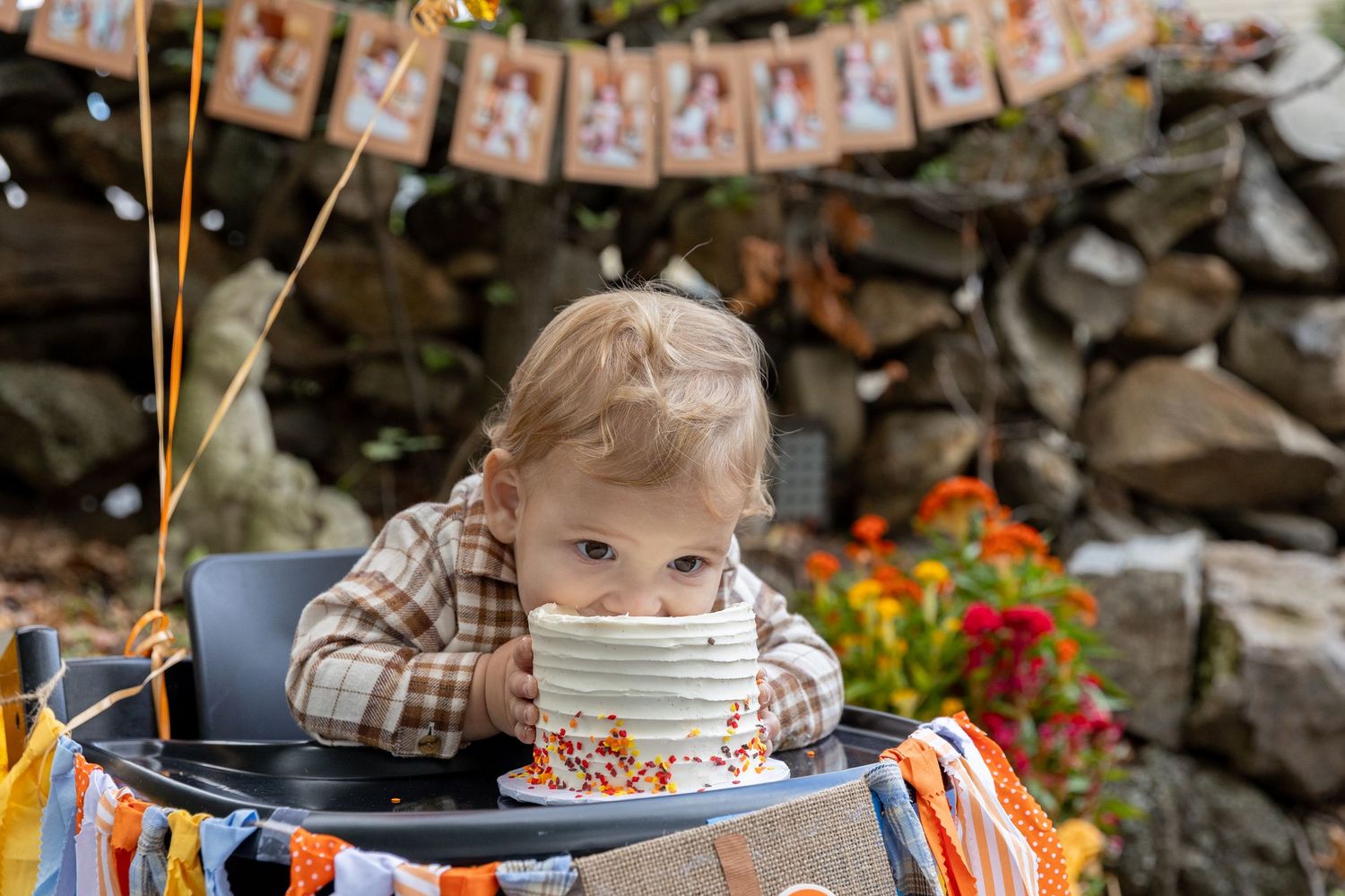 One-year-old baby tasting first birthday cake in high chair with fall-themed party decorations.