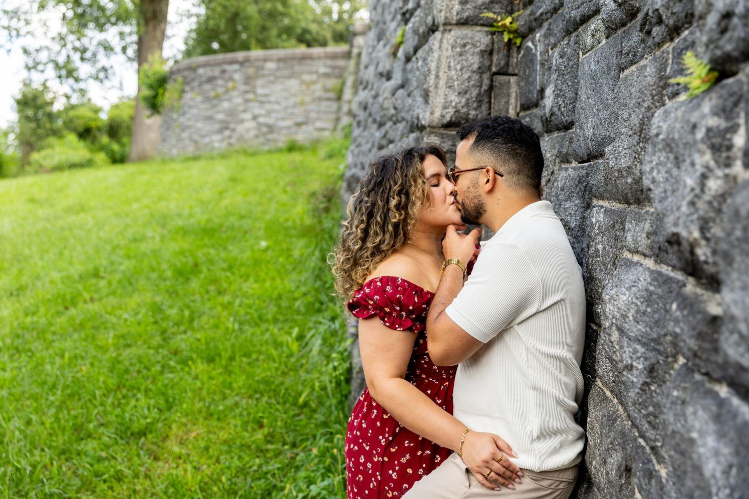 Romantic couple in colorful attire sharing intimate moment against rustic stone wall outdoors.