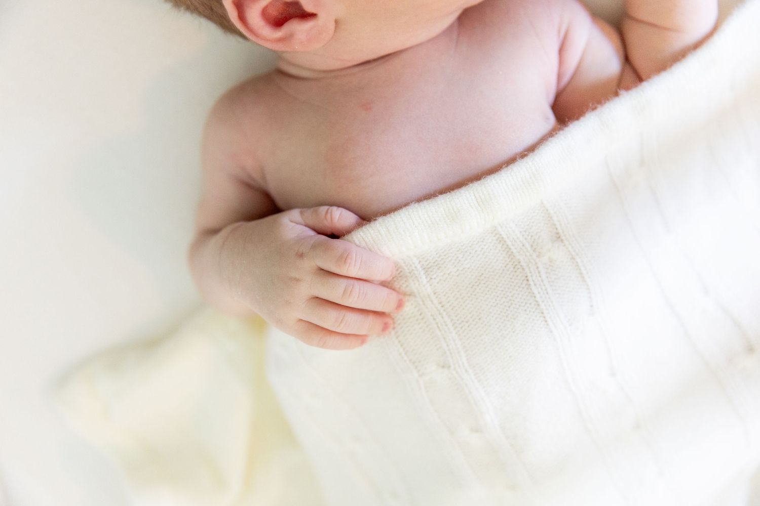 Close-up of a peaceful newborn baby wrapped in a soft white muslin swaddle blanket.