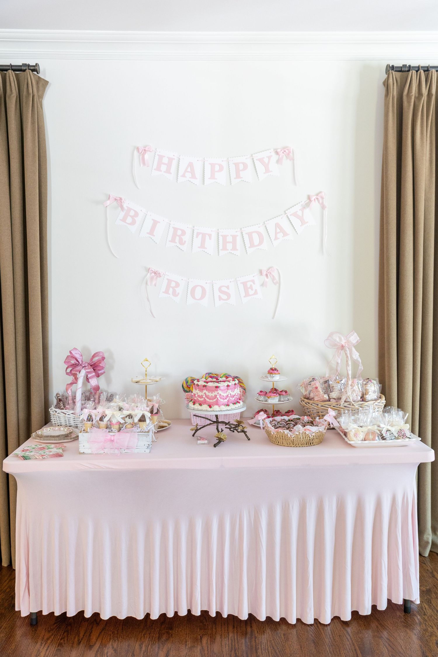 Pink and white Happy Birthday Rose banner above a decorated dessert table with cakes and sweets.