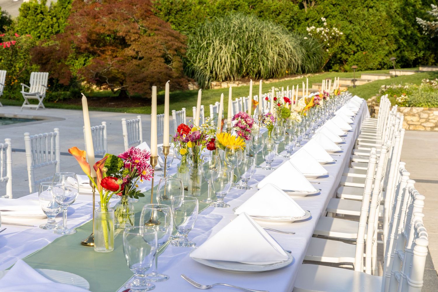 Long outdoor dining table with white linens, candles and colorful floral arrangements.