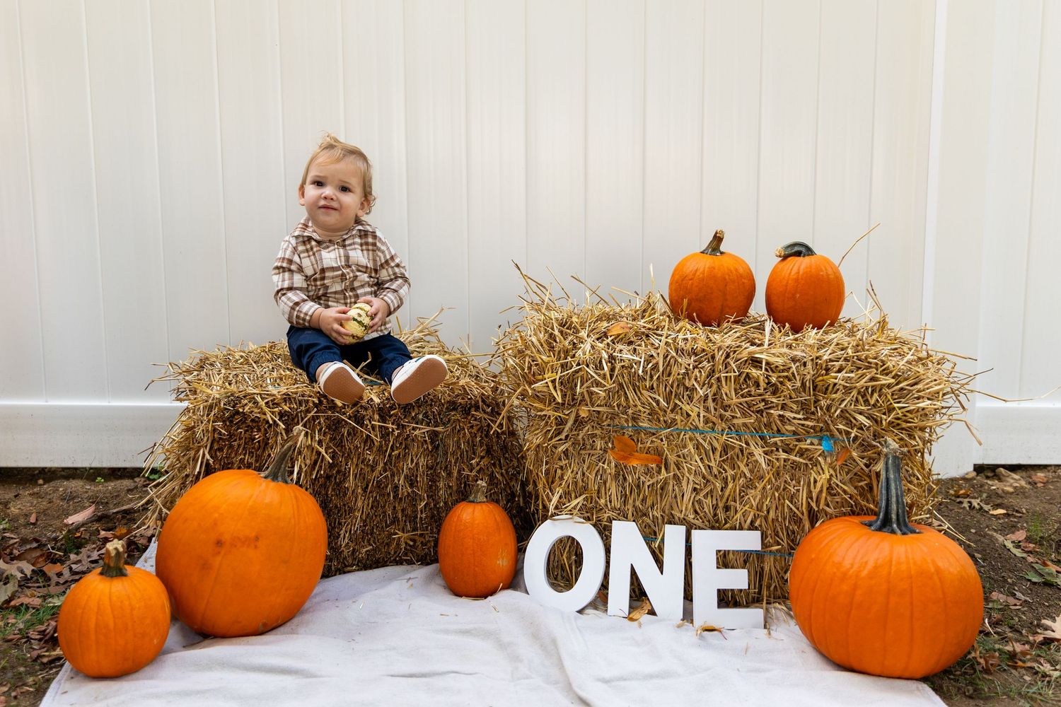 Baby's first birthday photo with hay bales, pumpkins, and ONE sign for a fall harvest theme.