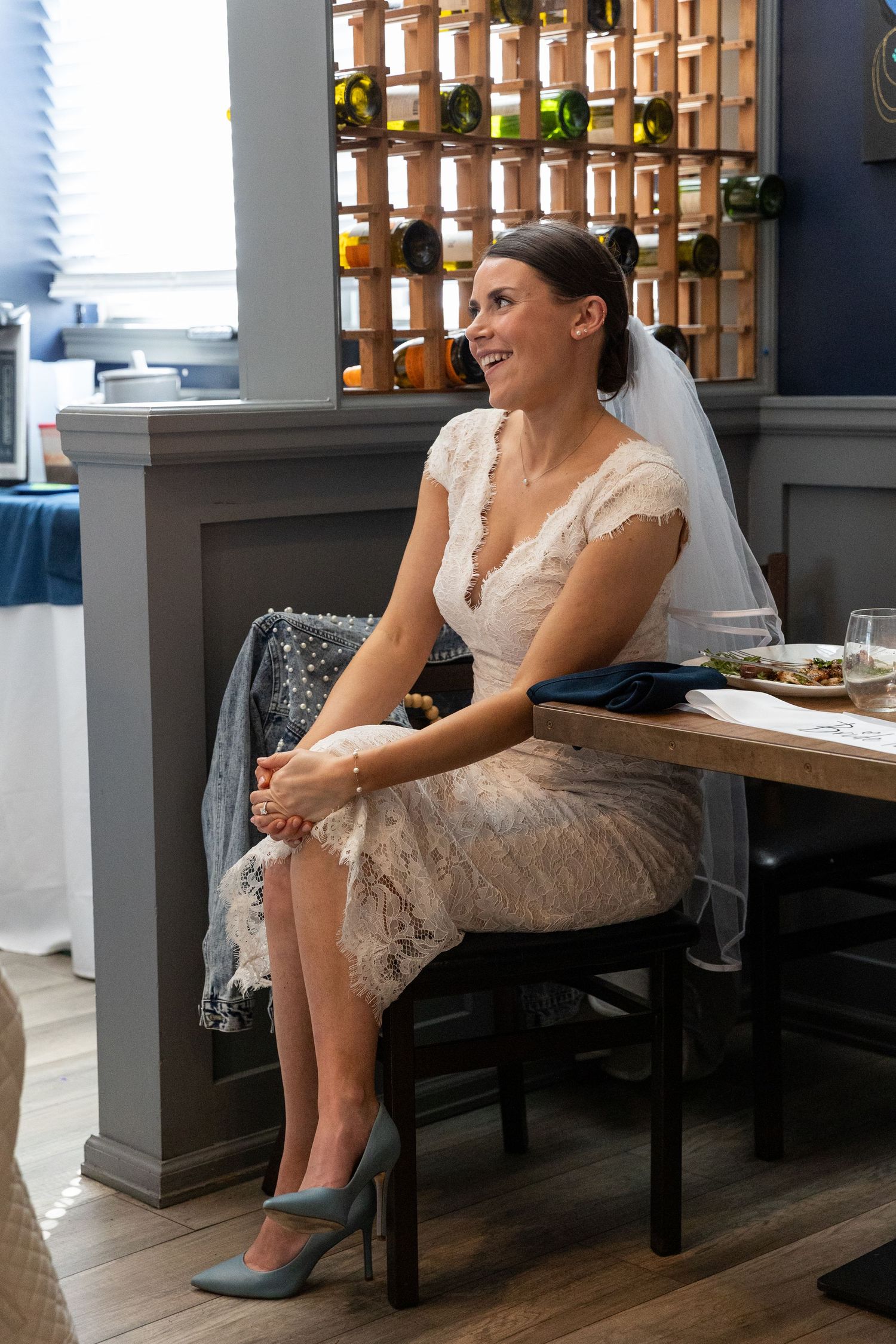 Smiling bride in lace dress and veil seated at restaurant during bridal shower.
