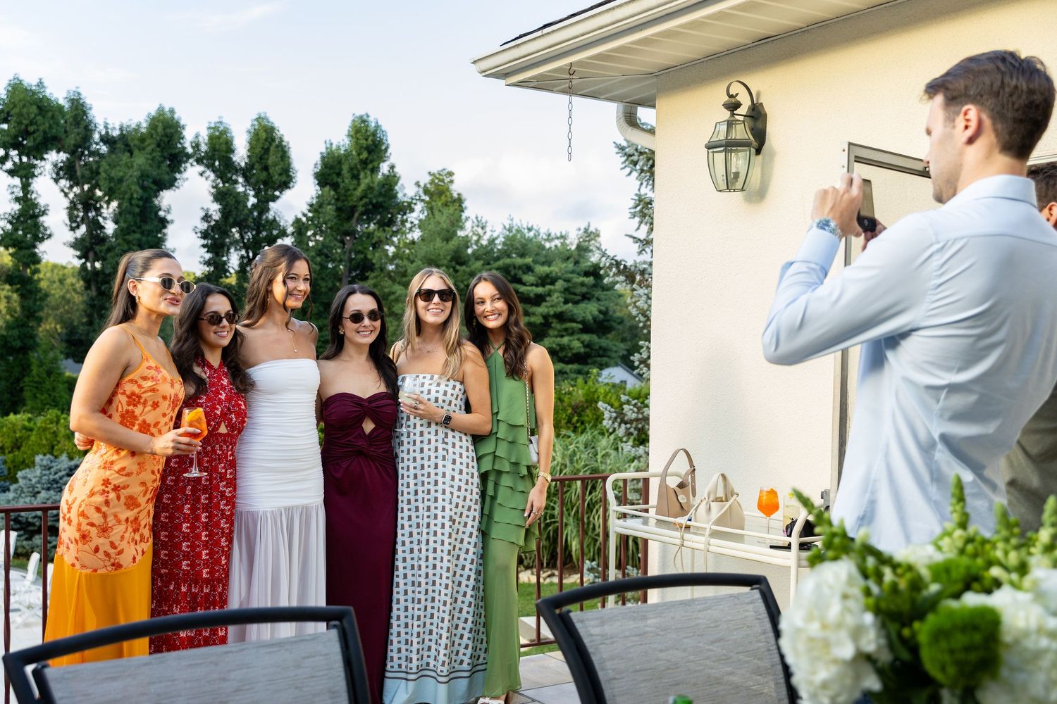 Man photographing group of women in colorful dresses on outdoor balcony.