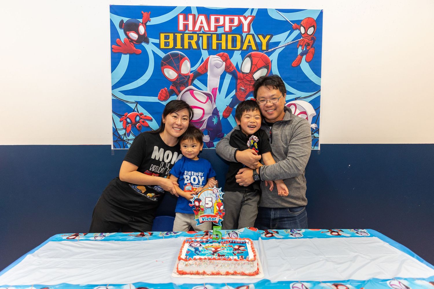 Happy family of four posing in front of Spiderman birthday backdrop with cake.