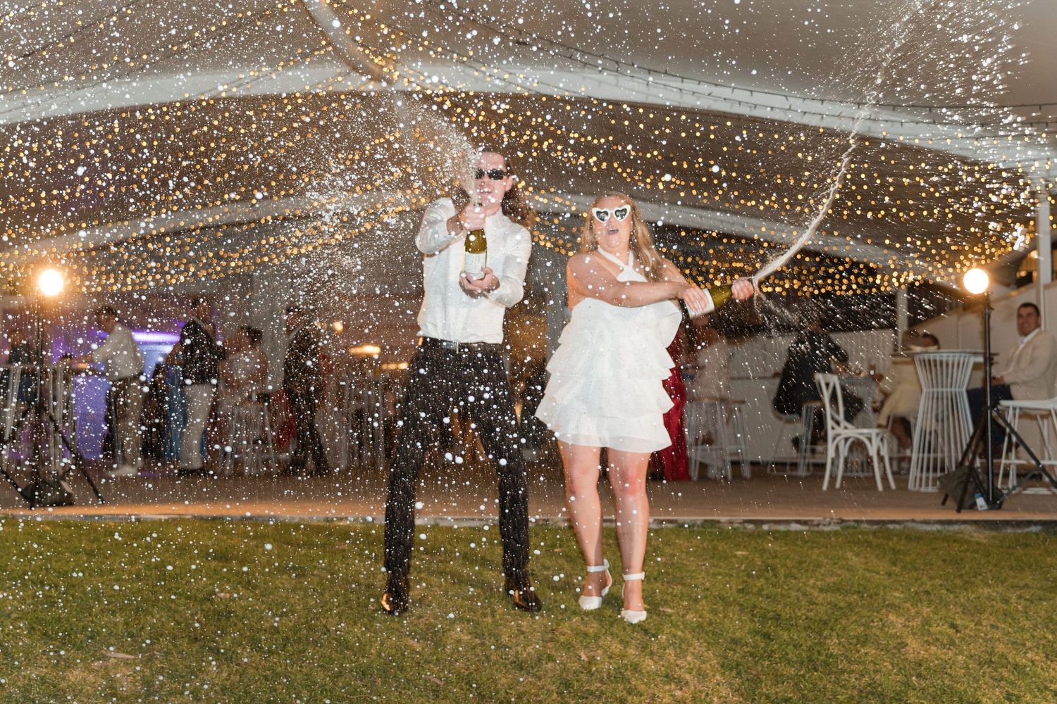 Bride and groom dance under confetti shower at elegant tented wedding reception at night.