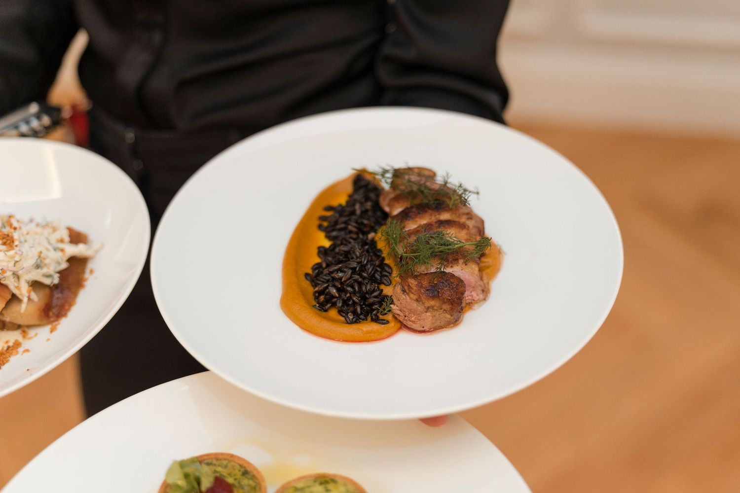 Gourmet meat dish with black sauce and orange puree plated elegantly on white china.