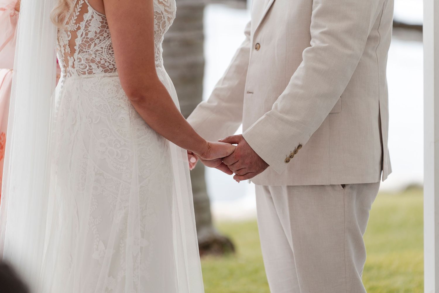 Close-up of couple holding hands during waterfront wedding ceremony.