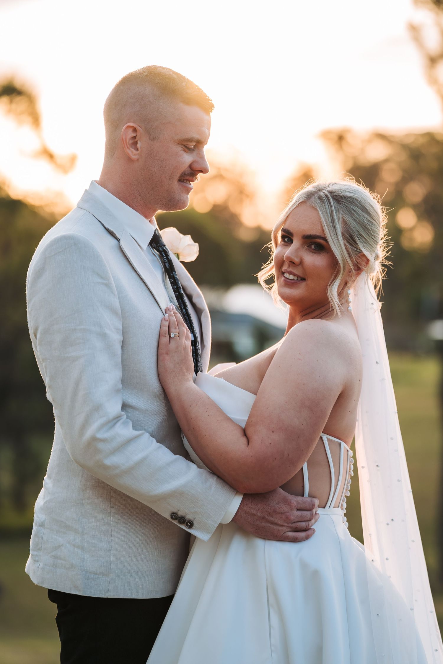 A romantic sunset portrait of newlyweds embracing in formal wedding attire at their outdoor ceremony.