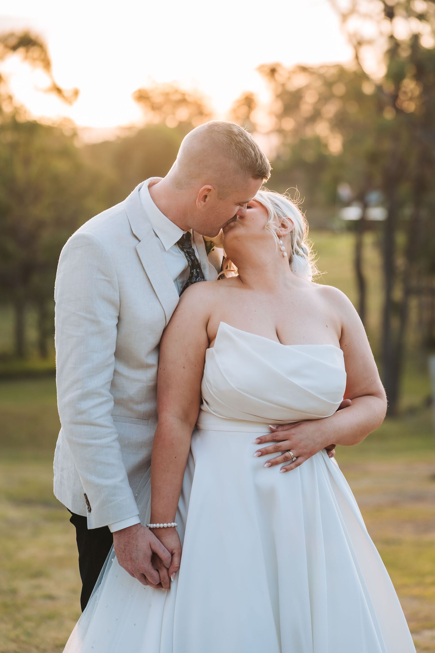 A romantic wedding couple share a tender moment at sunset in a garden setting while dressed in elegant white attire.