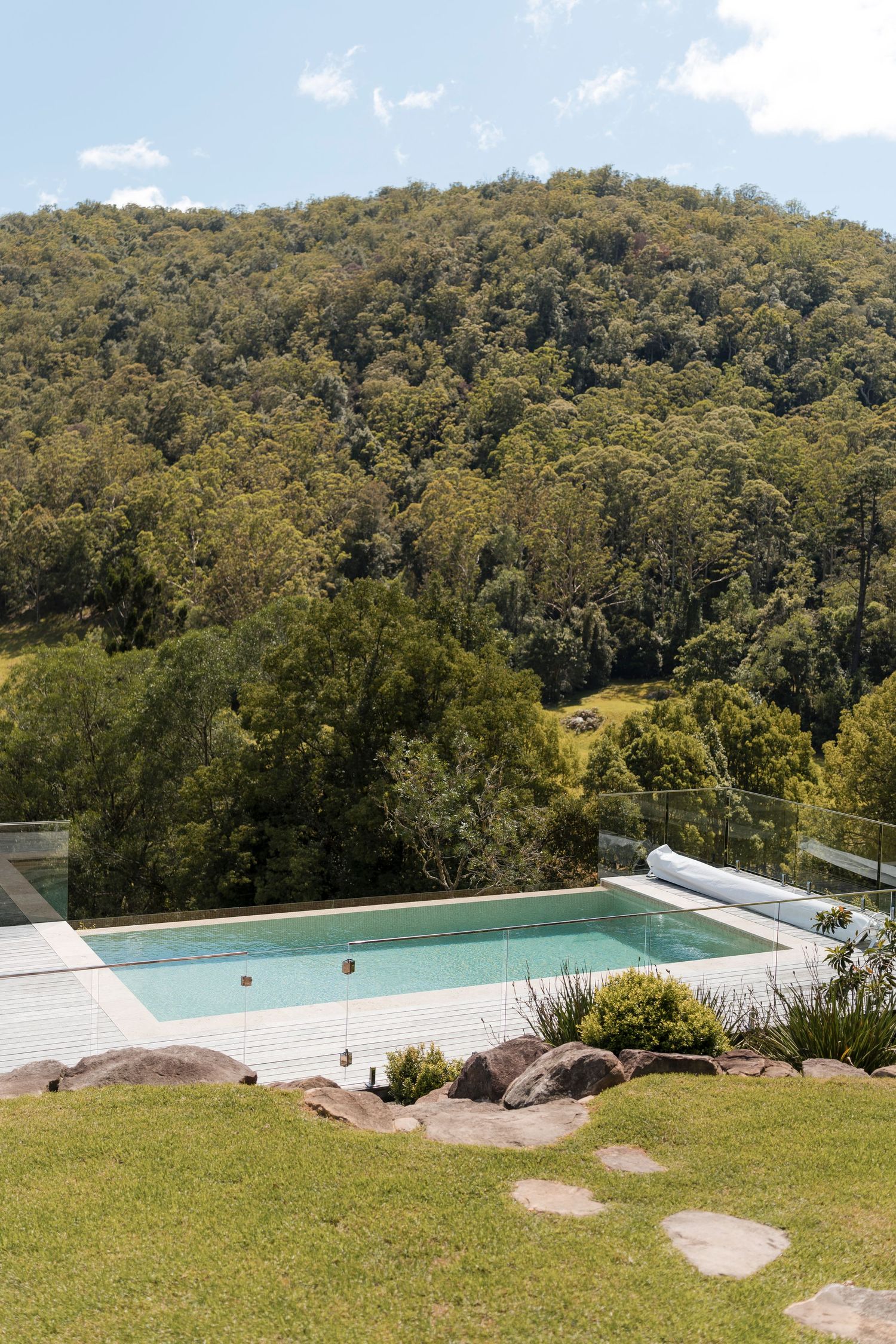 Modern infinity pool with mountain views nestled in lush green hillside setting with stone path and landscaped garden.