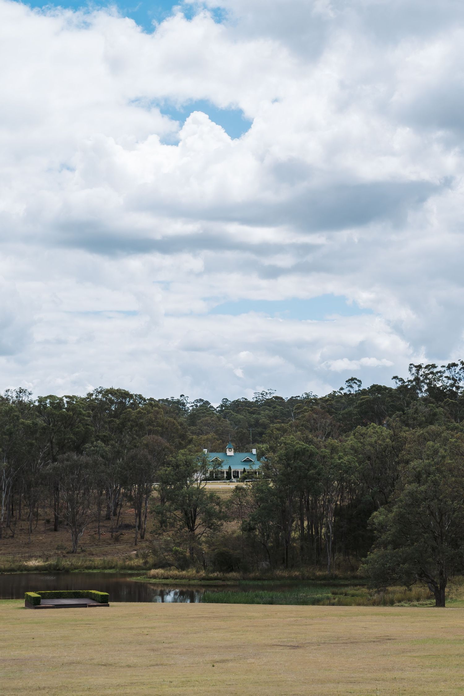 A green house sits atop a hill surrounded by Australian bushland with cloudy skies overhead.
