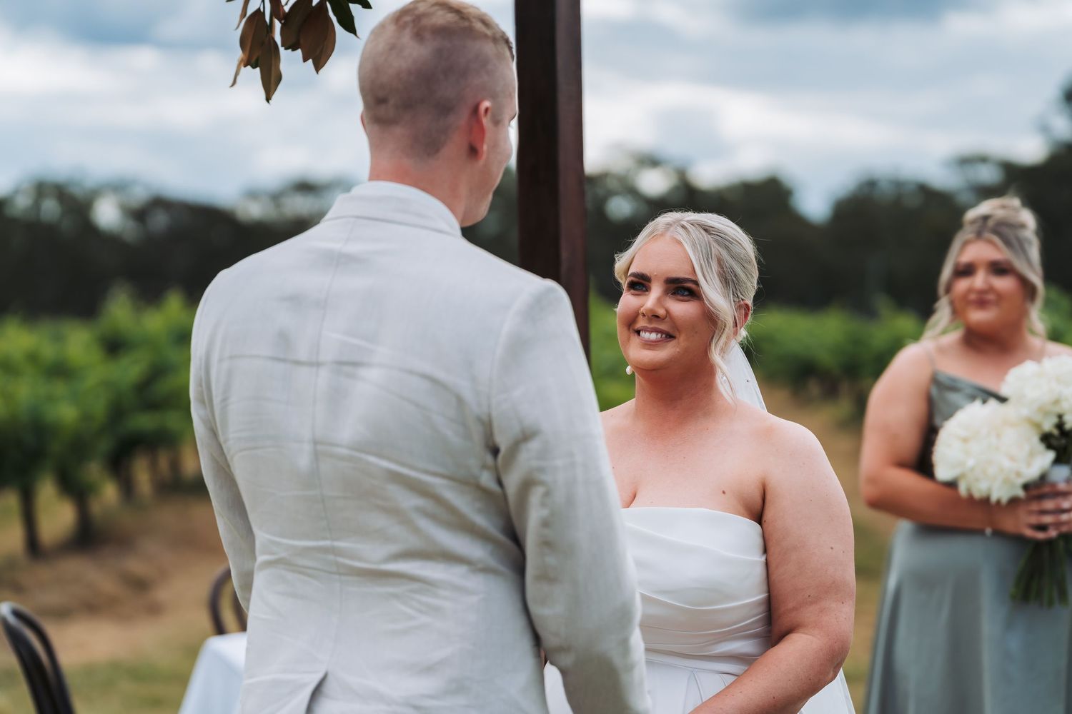 Wedding ceremony taking place at a scenic vineyard with guests watching the exchange of vows.