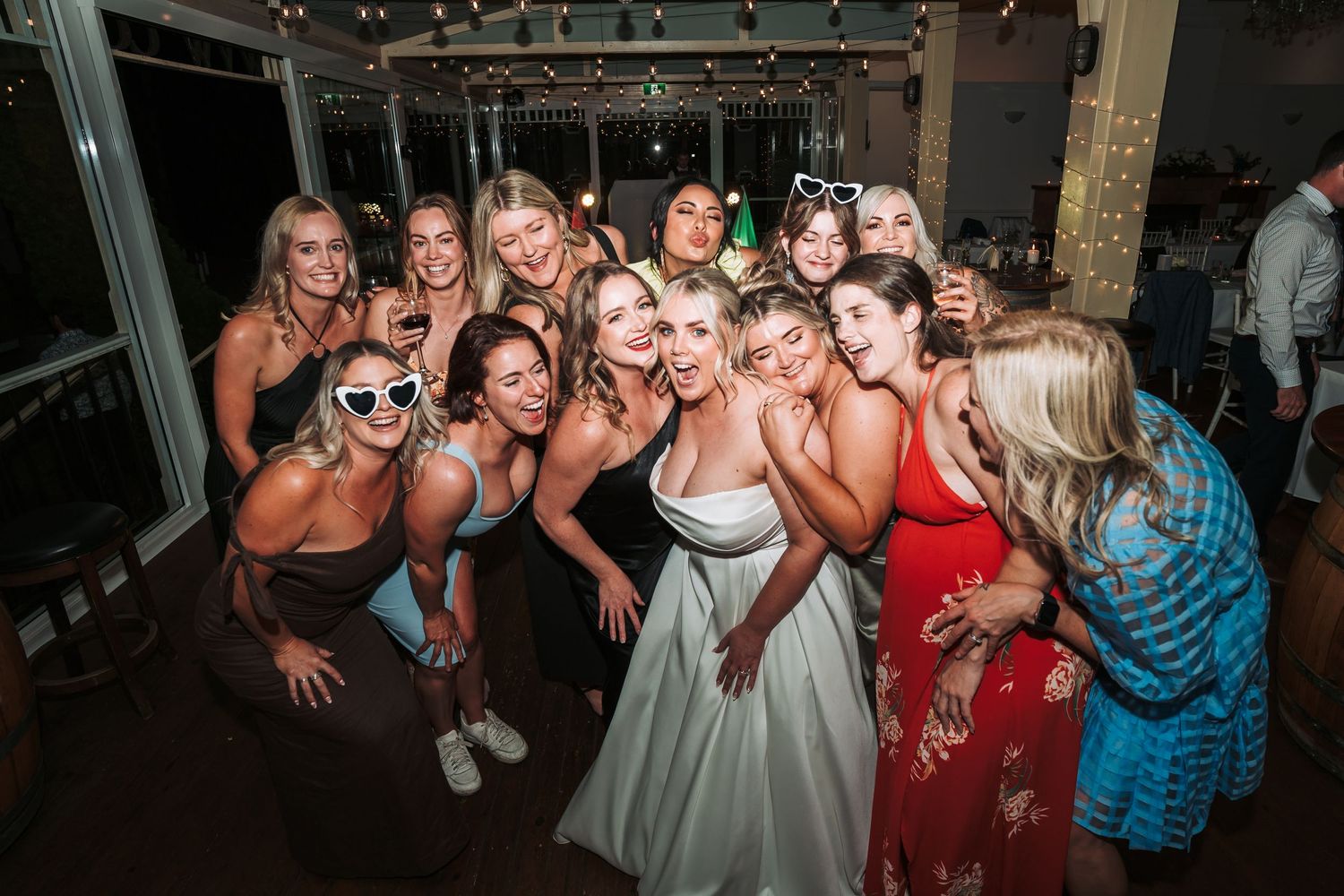 Wedding party group poses together during reception celebration with festive expressions.