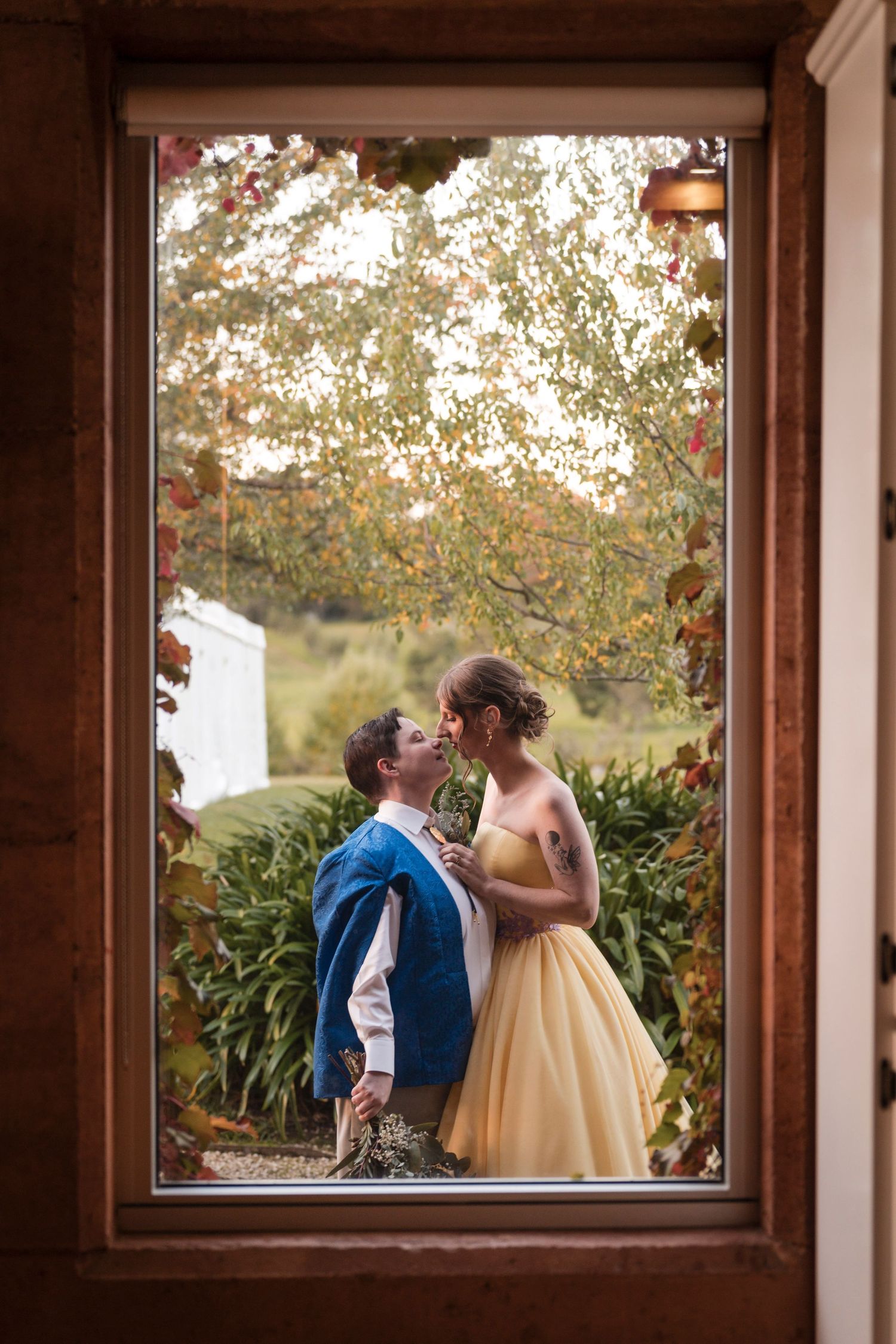 A romantic moment framed through a wooden window with autumn foliage in the background.