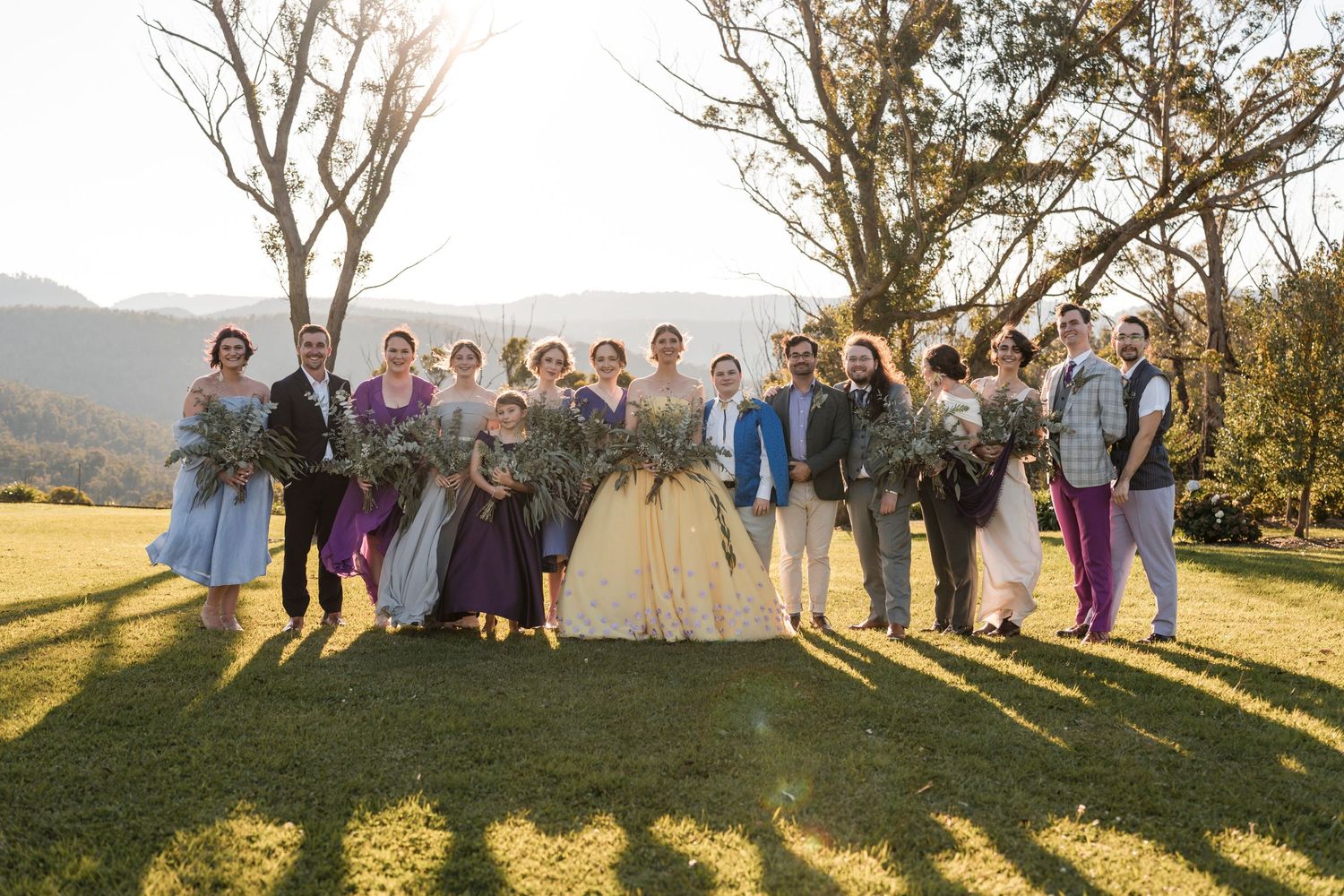 Wedding party poses together on a scenic hilltop during golden hour at an outdoor mountain venue.