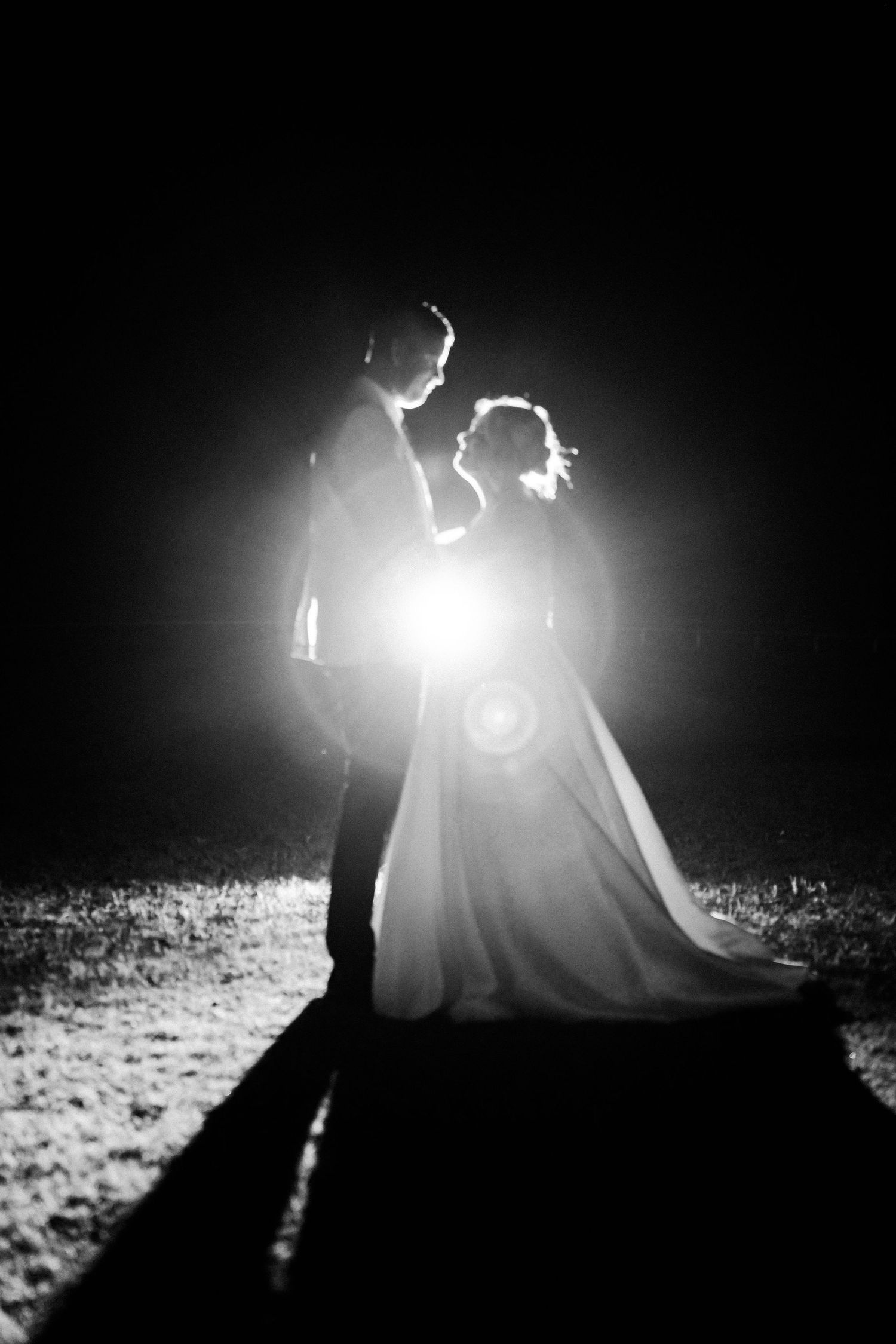 Silhouette of couple in wedding attire backlit against bright light creating dramatic effect.