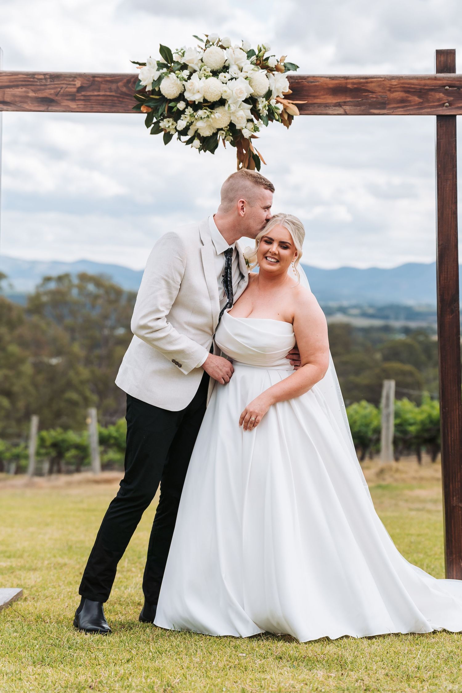 A couple shares a joyful moment under a floral arch at their outdoor wedding ceremony in a scenic mountain setting.