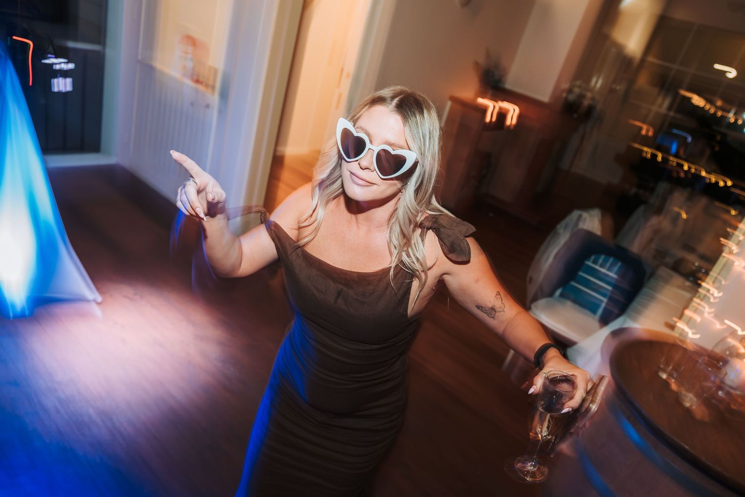 Person dancing at a party with sunglasses in a dark room with blue lighting.