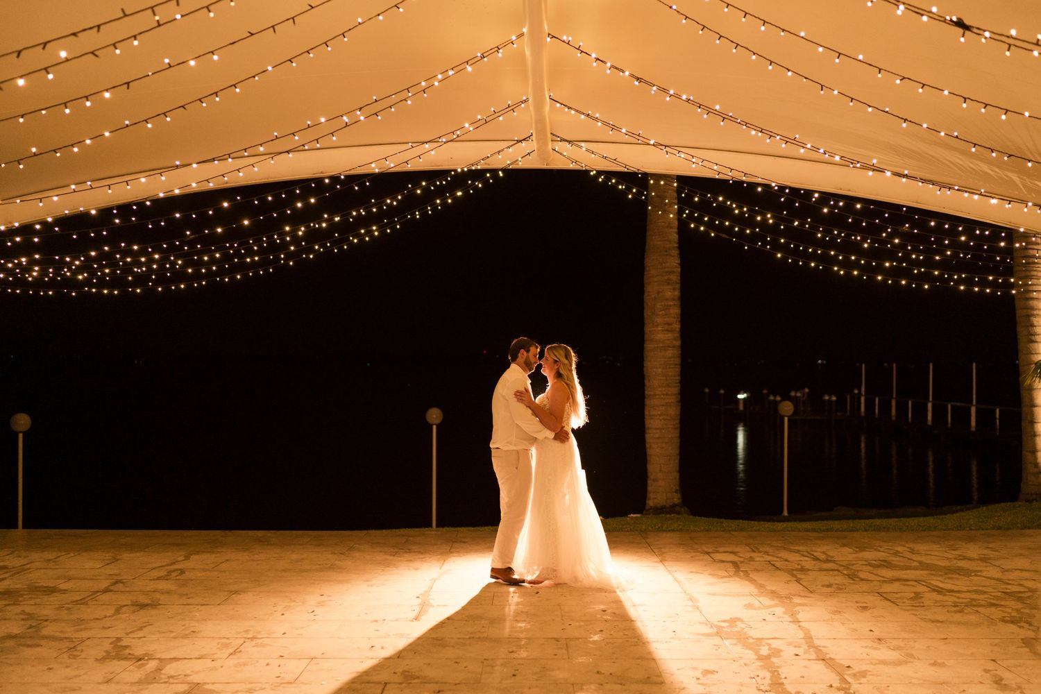 A romantic silhouette of a dancing couple under twinkling lights in an outdoor wedding tent.