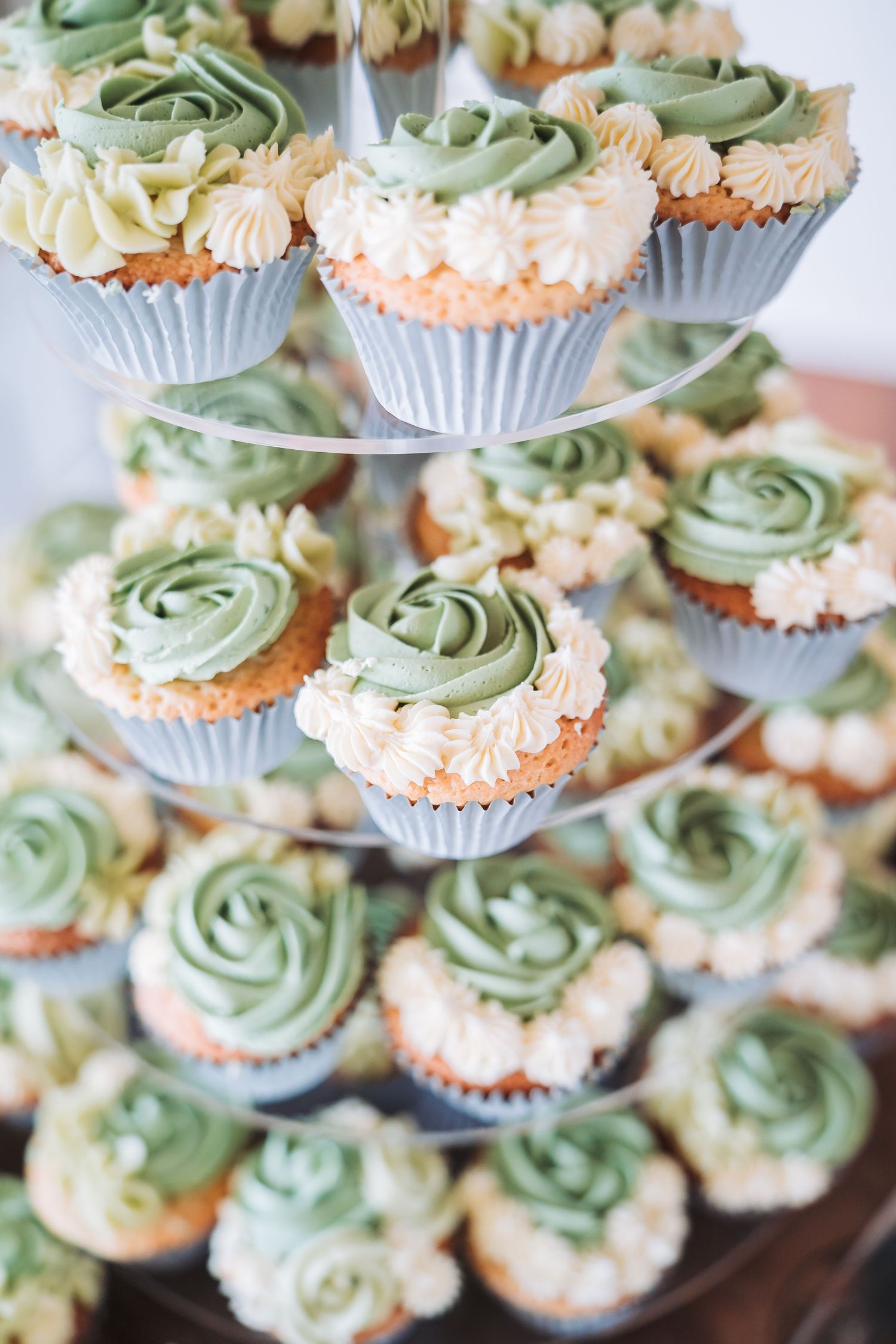 Elegant tiered display of cupcakes with mint green frosting swirls and peach-colored decorative details.