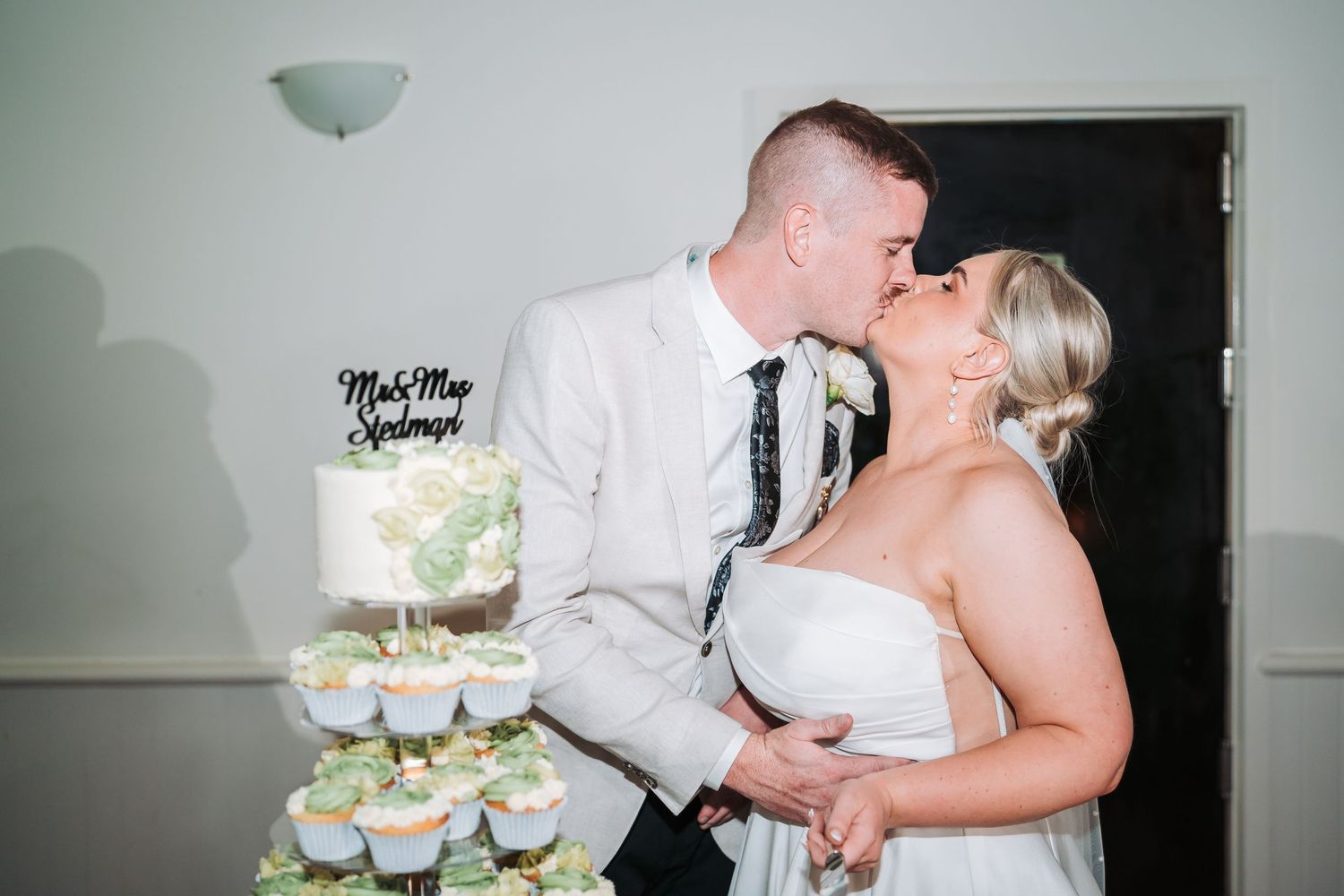 Newlywed couple shares intimate kiss beside tiered wedding cake display with 