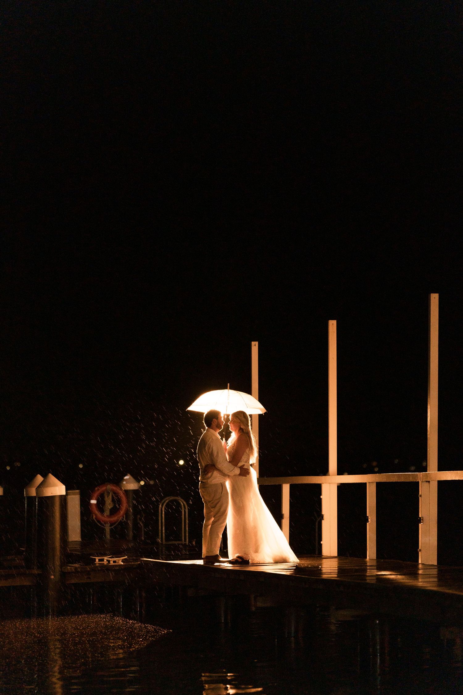 A couple shares an intimate moment under a lit umbrella on a dock at night.