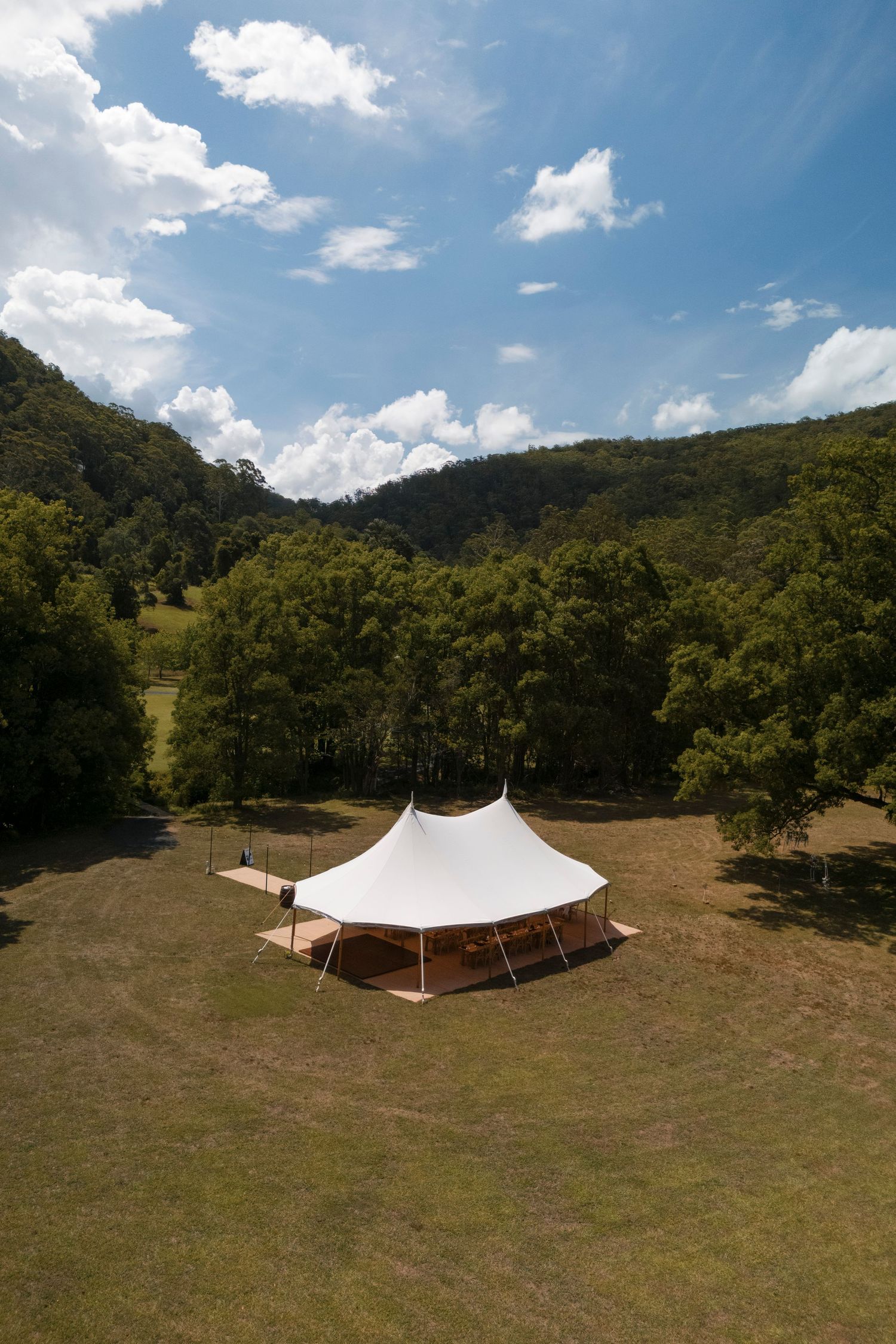 Aerial view of a large white tent in a scenic valley surrounded by forested hills.
