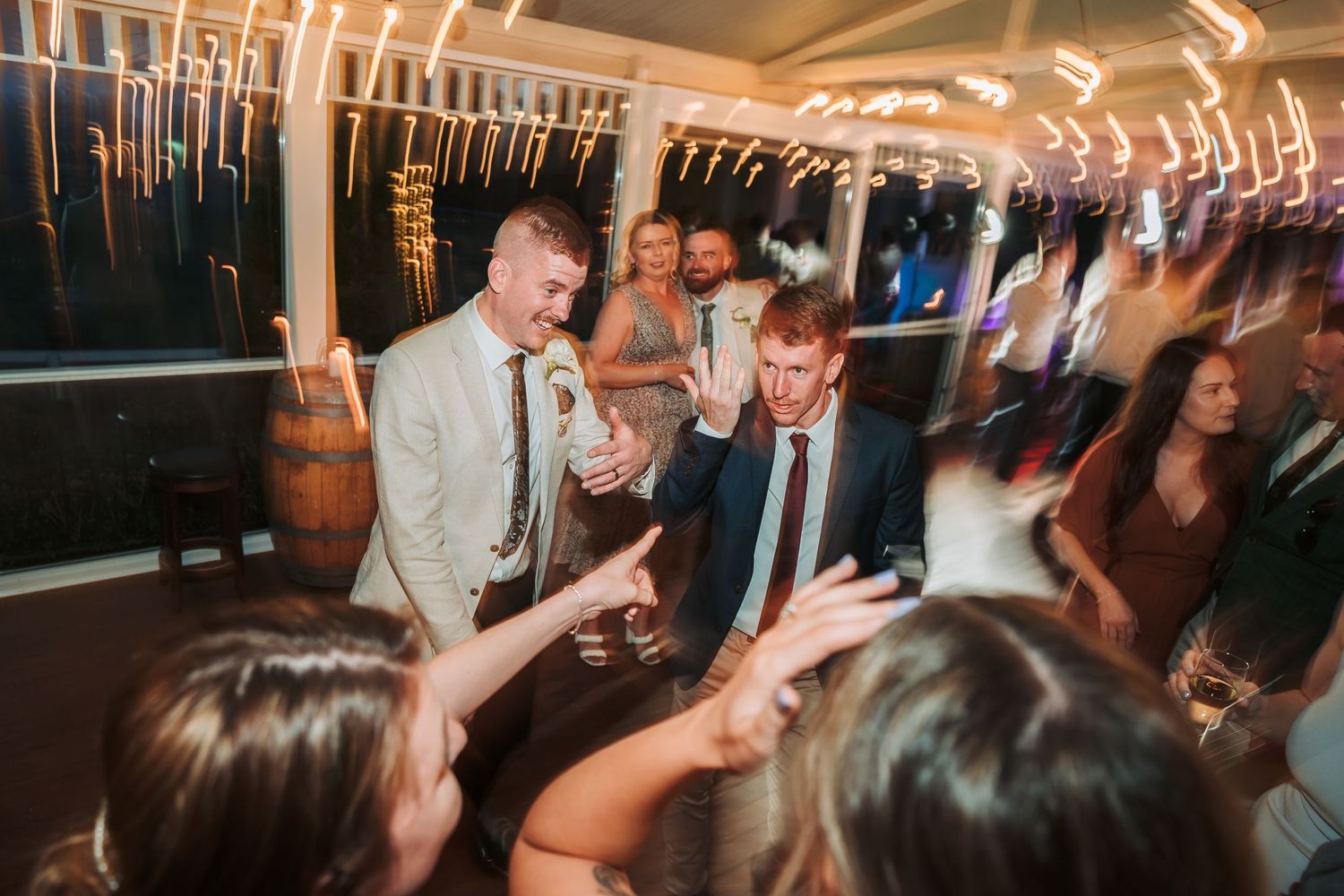 Wedding guests dancing energetically at an indoor party with light trails creating a dynamic atmosphere.