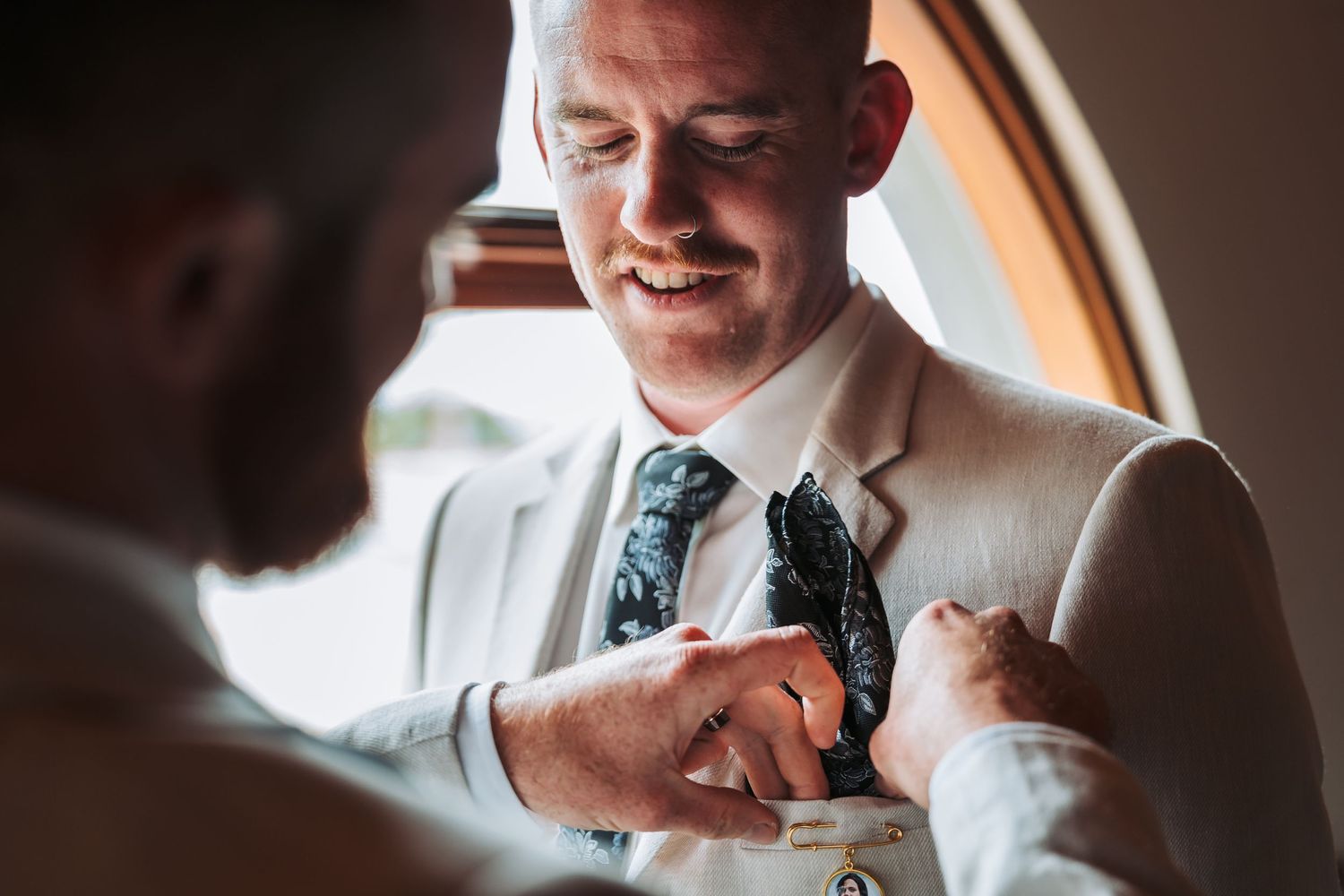 A close-up shot of formal attire being adjusted with a floral tie and light colored suit.