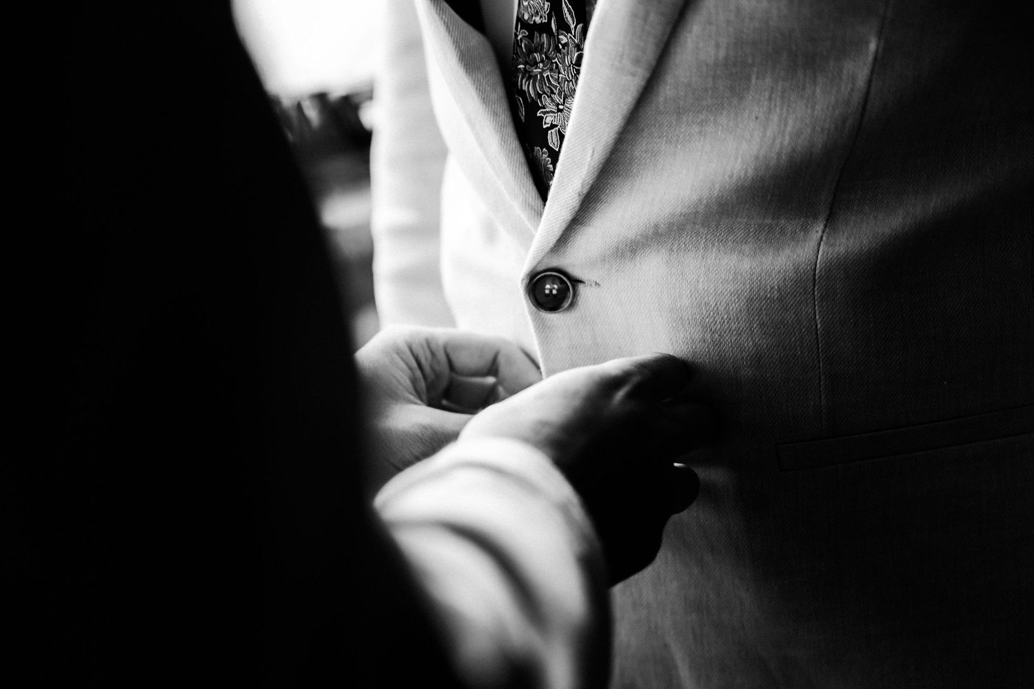 Close up black and white detail of formal suit jacket button and fabric.