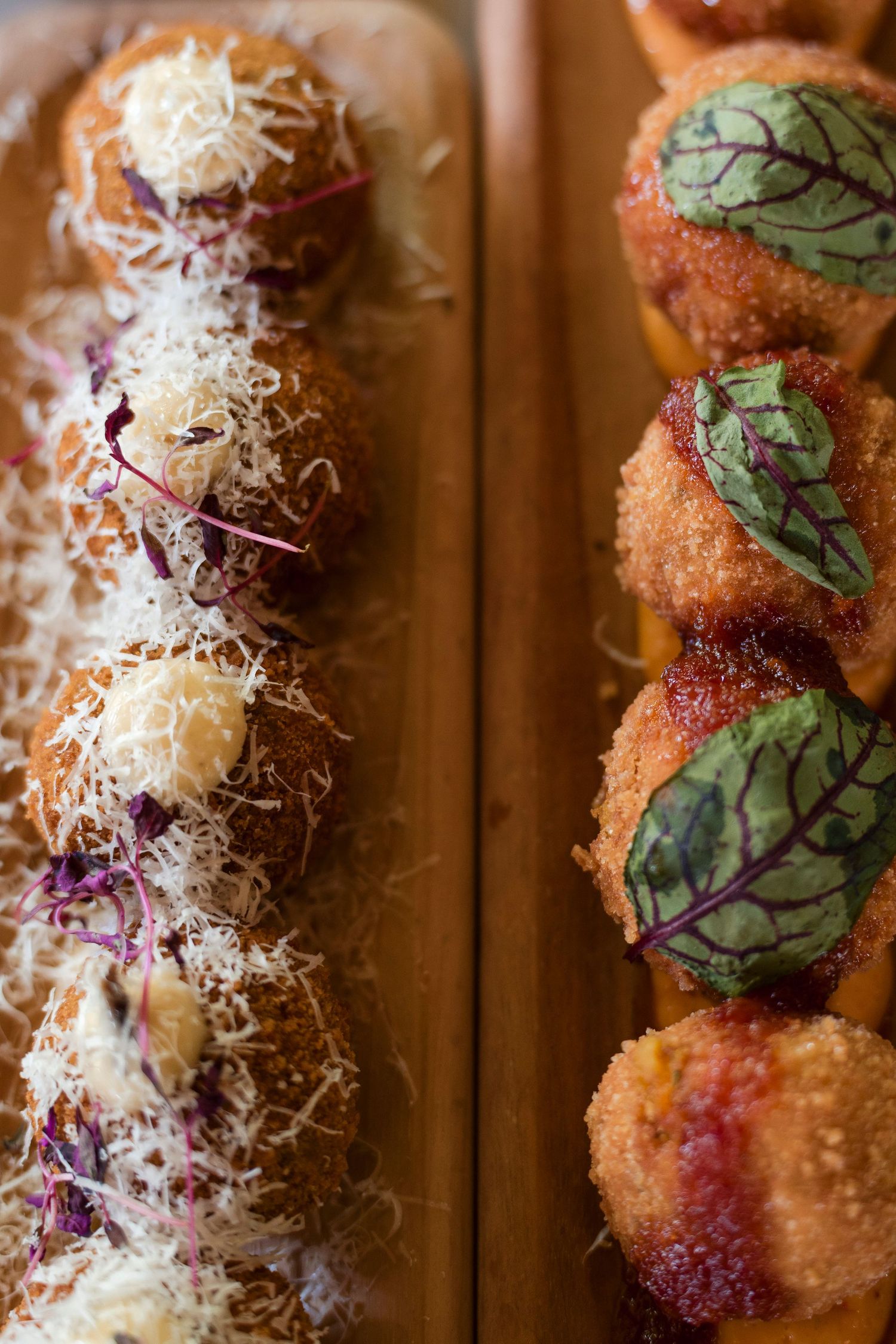Close-up shot of two rows of Italian arancini appetizers, one topped with shredded cheese and one with fresh basil leaves.