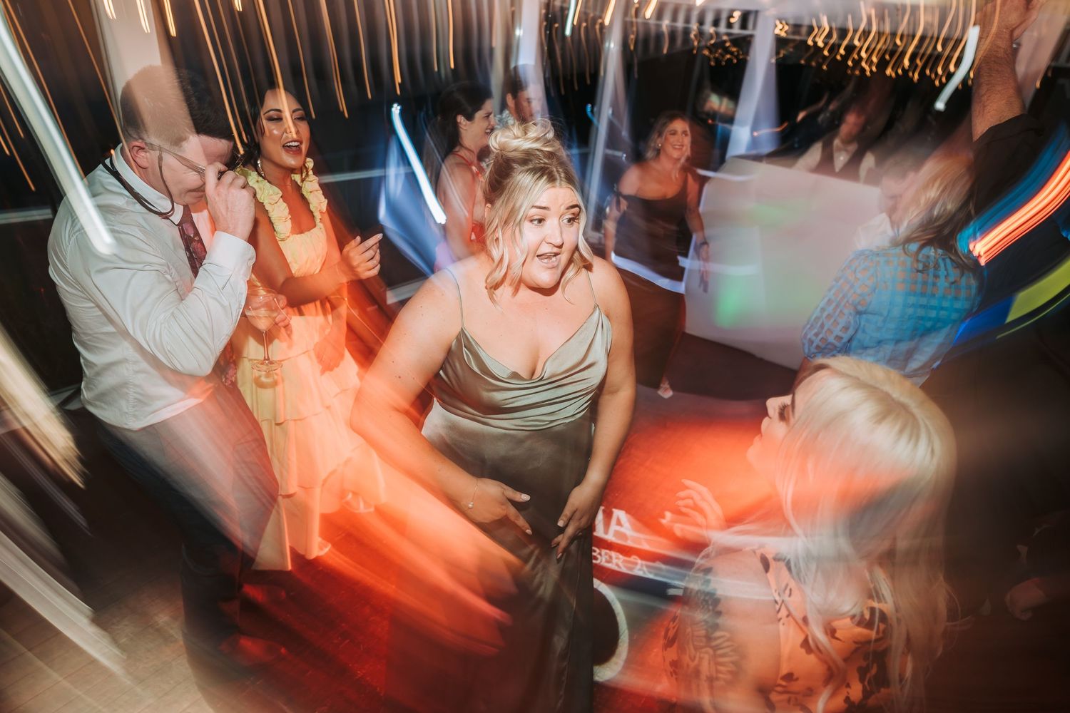 Motion-blurred shot of wedding guests dancing under orange and blue lighting at a reception.