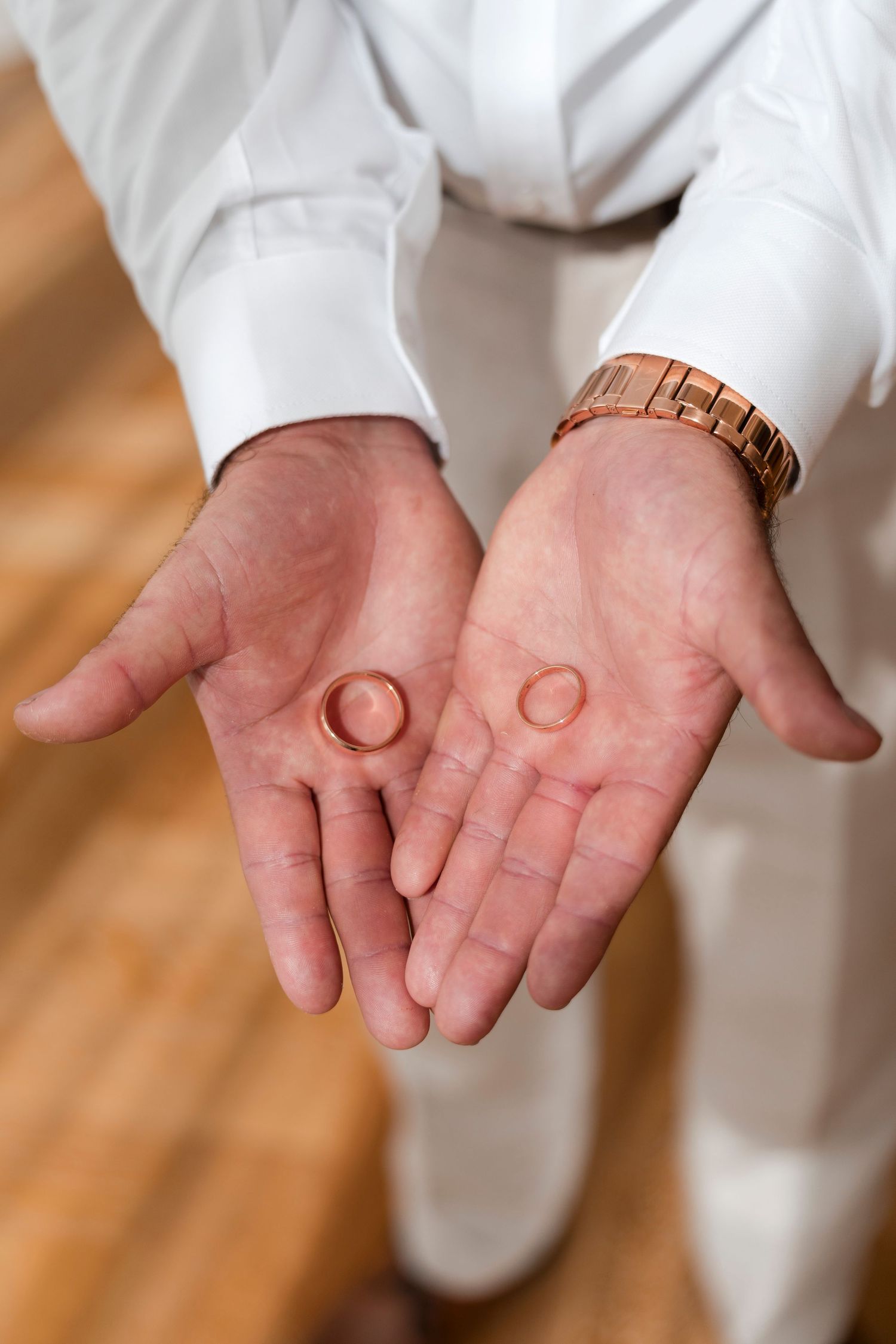 Two wedding rings held in open palms wearing white formal attire.