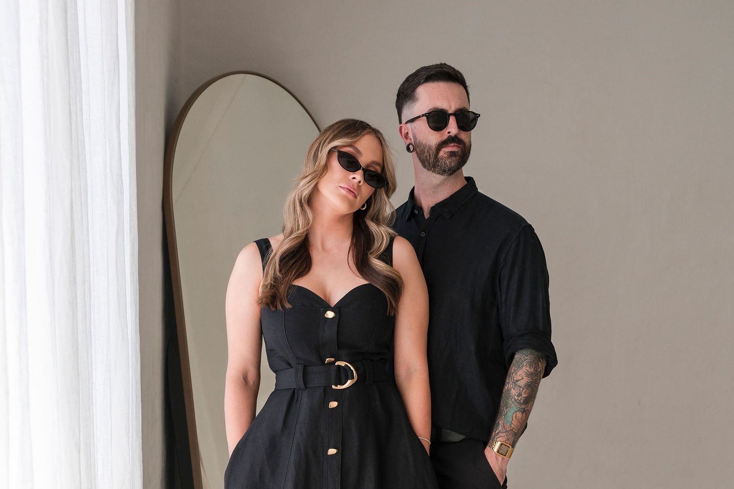 Male and female wedding photography duo pose together in matching black outfits in studio.