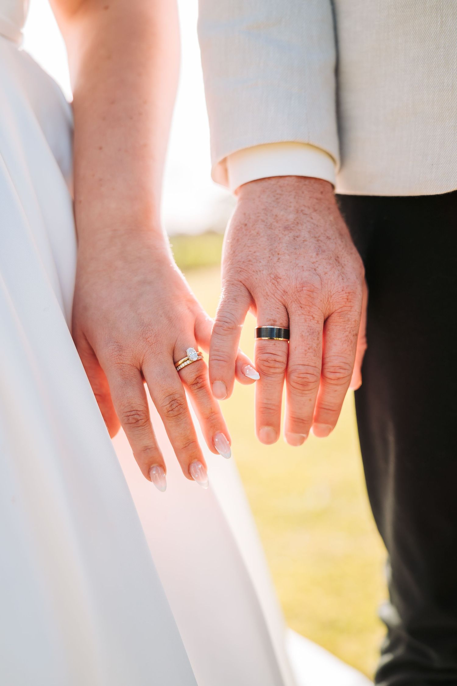 Close-up of newlywed couple's hands showing matching wedding bands in golden sunlight.