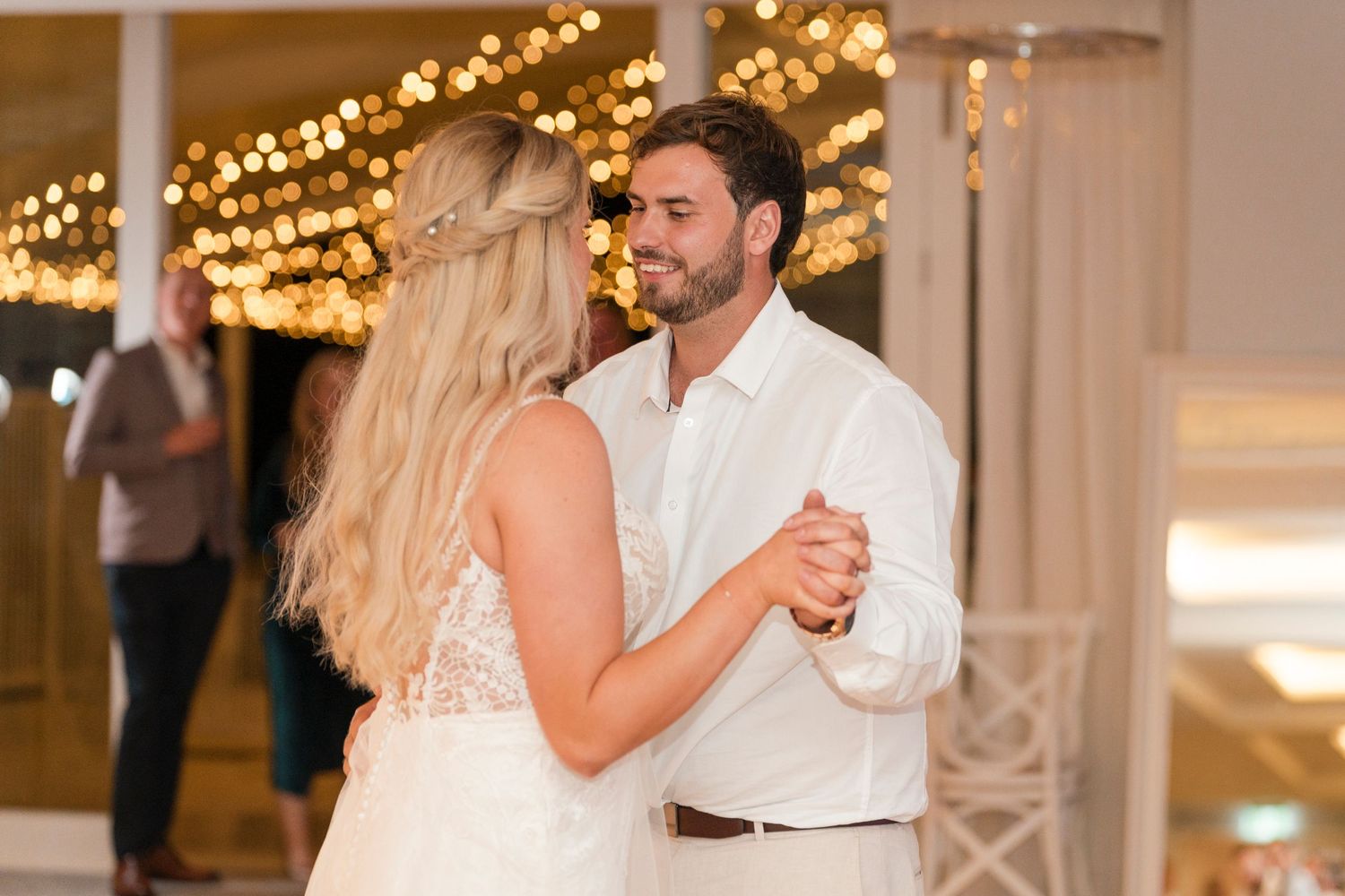 Intimate dance moment under warm string lights at wedding reception.