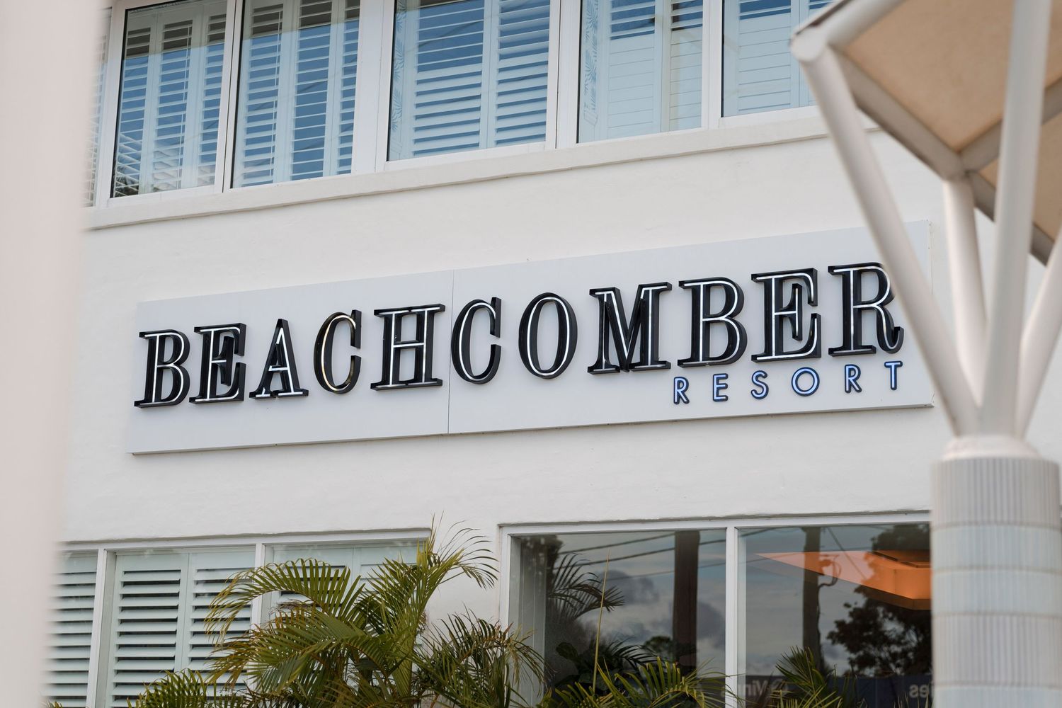 White building exterior signage reading 'Beachcomber Resort' with shuttered windows and palm fronds.