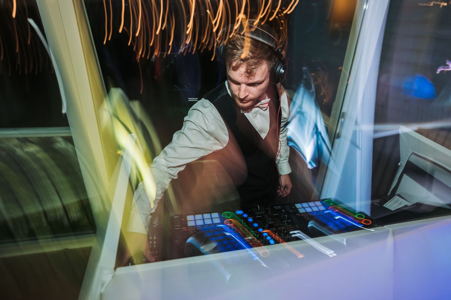 A DJ performs at a nightclub booth, illuminated by blue lights while working with professional mixing equipment.