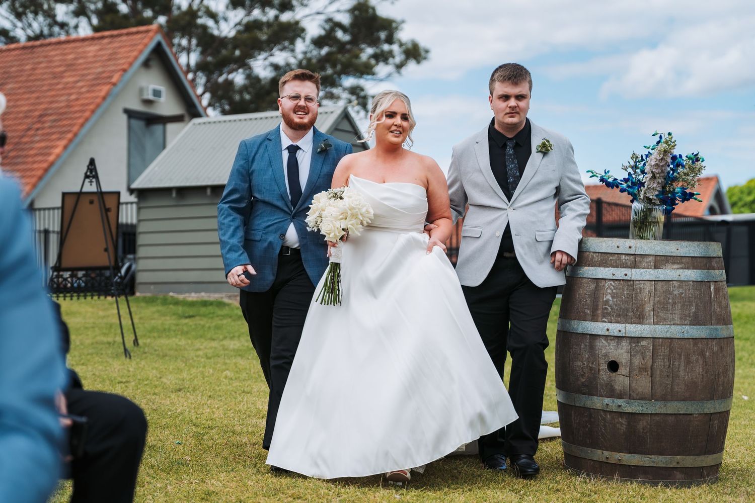 Wedding party gathered near rustic wine barrel during outdoor countryside celebration.
