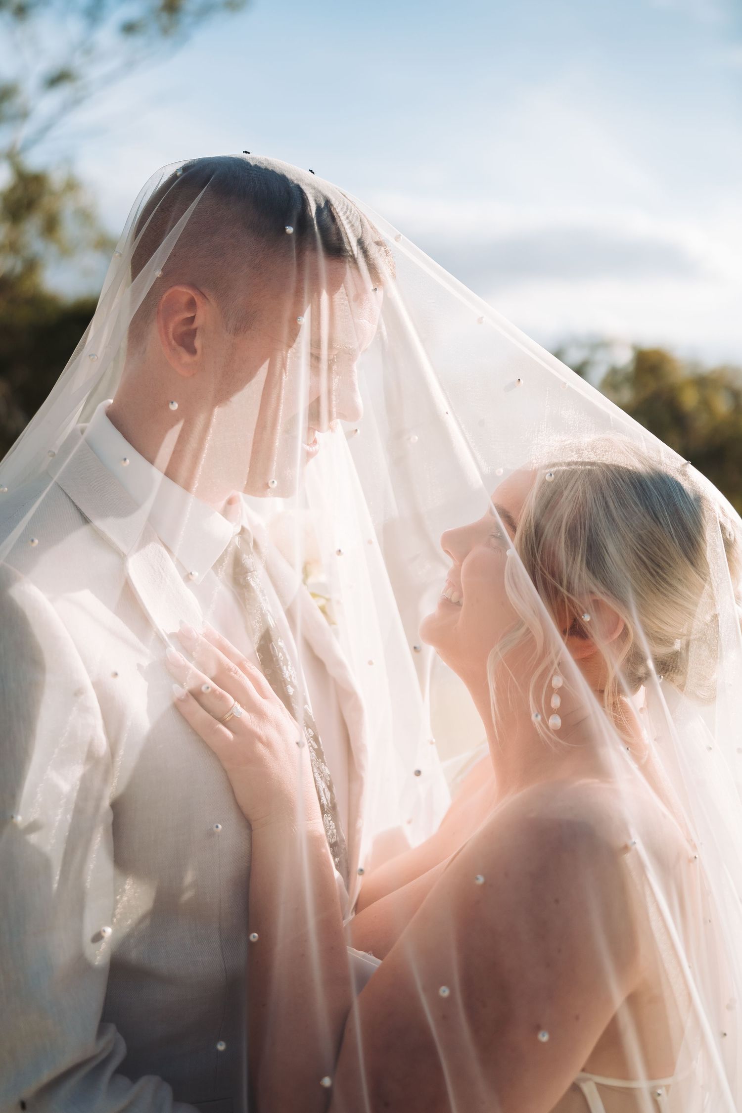 A romantic wedding moment captured through a delicate veil with soft sunlight creating a dreamy atmosphere.