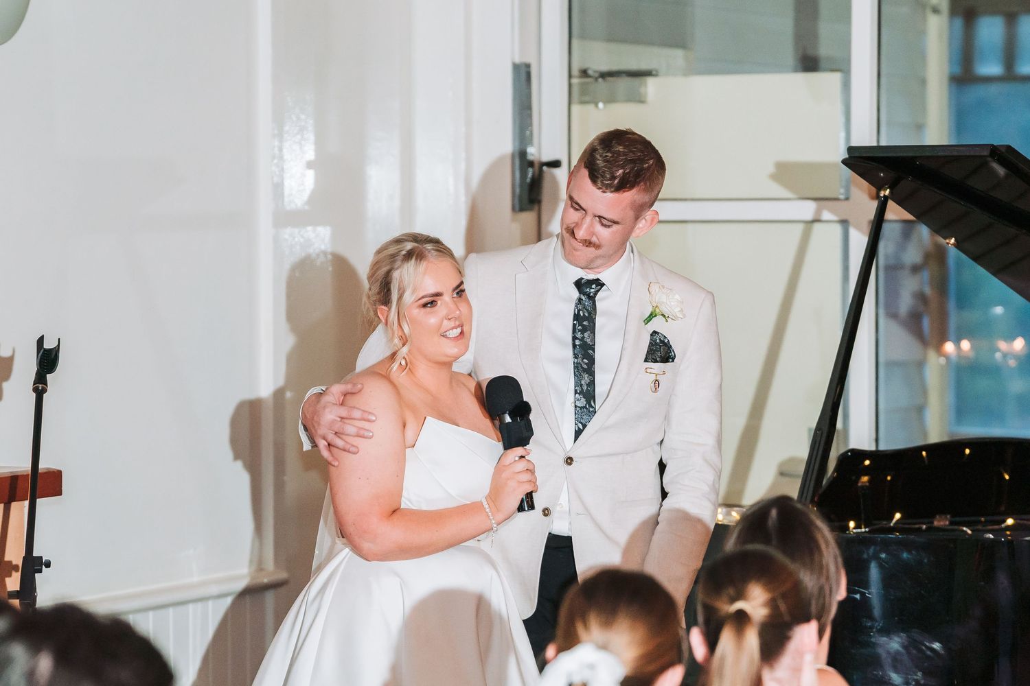 Couple shares an emotional moment during their wedding reception speech near a grand piano.