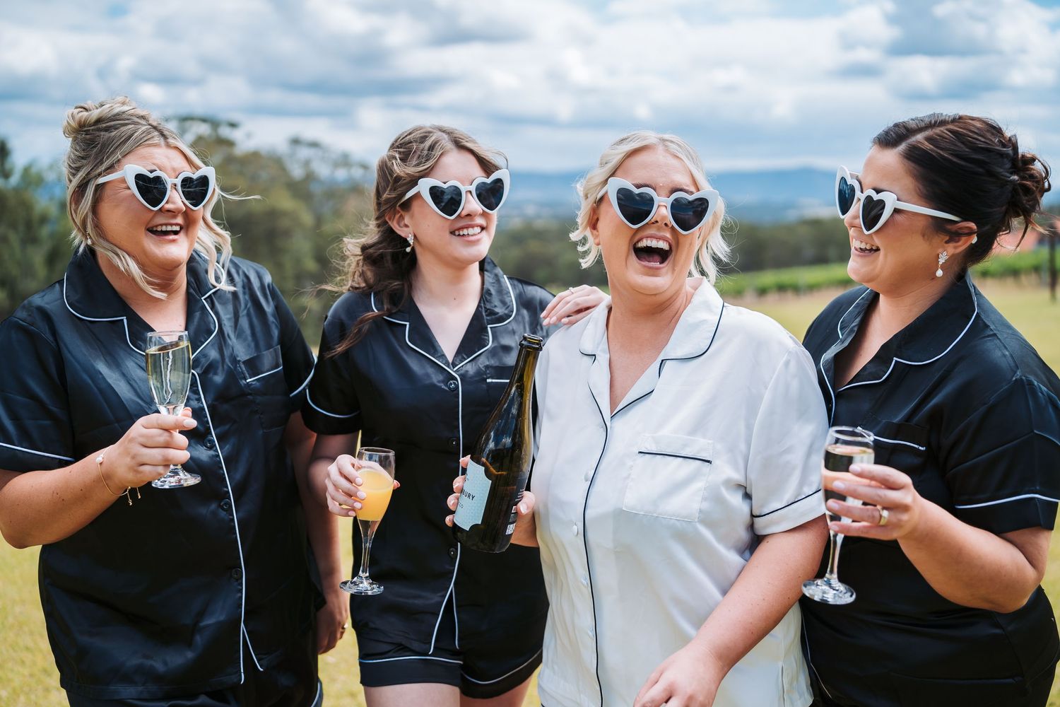 Bridesmaids in matching navy robes enjoying drinks and laughter outdoors.